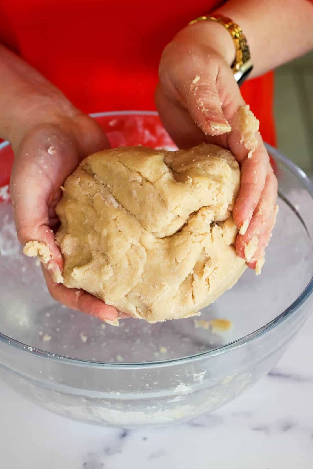 Hands forming the finished dough until it comes together in one cohesive ball.