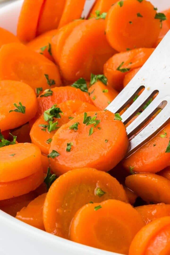 A fork lifting a slice of brown sugar and honey glazed canned carrots.