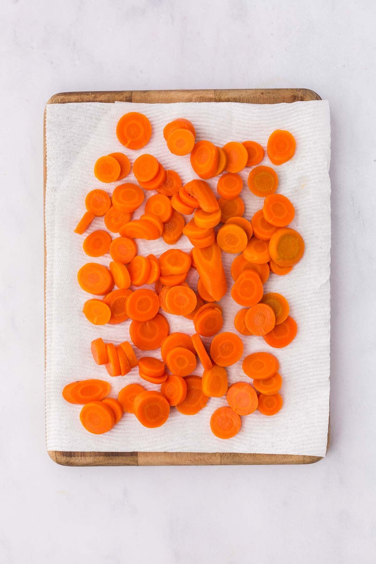 Sliced canned carrots drying on a paper towel-lined cutting board in preparation for glazing.