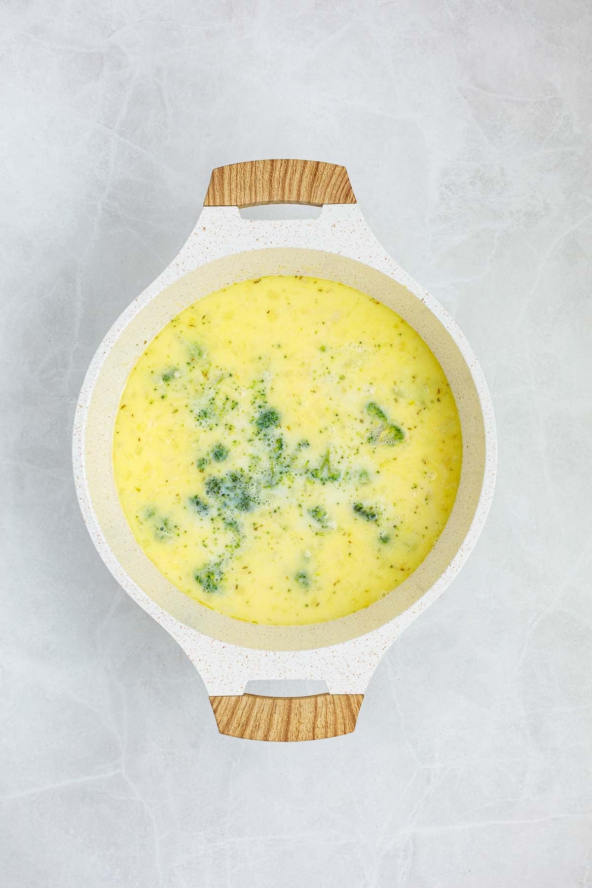 Broccoli added to the creamy soup base, starting to simmer in the pot.