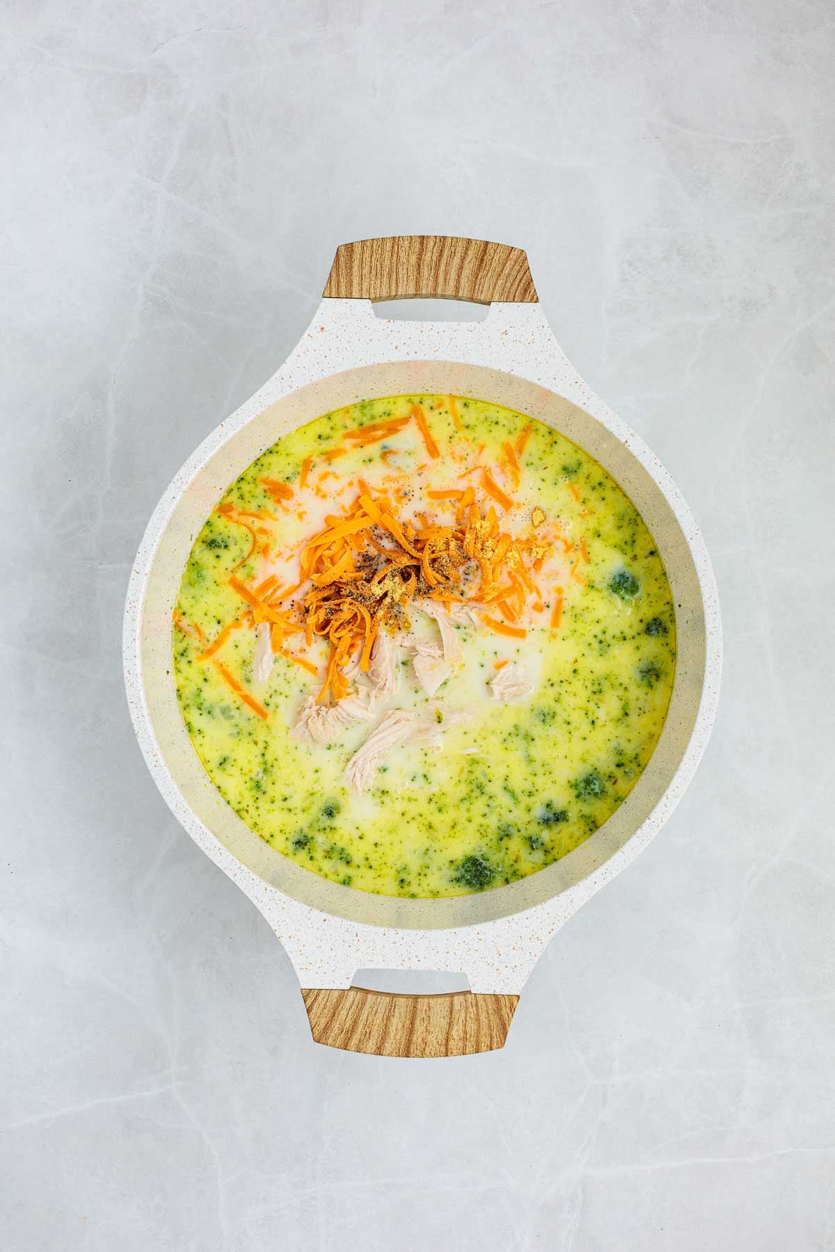 Chicken, shredded cheddar, and seasonings layered into the pot over the simmering broccoli soup mixture.