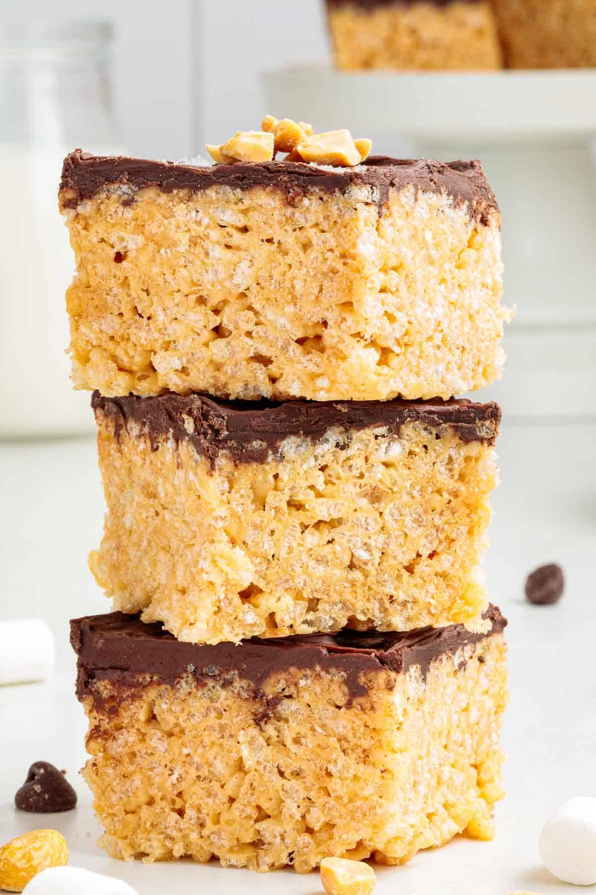 A stack of three thick chocolate-covered Rice Krispie treats with visible crispy cereal texture and chopped peanuts on top.