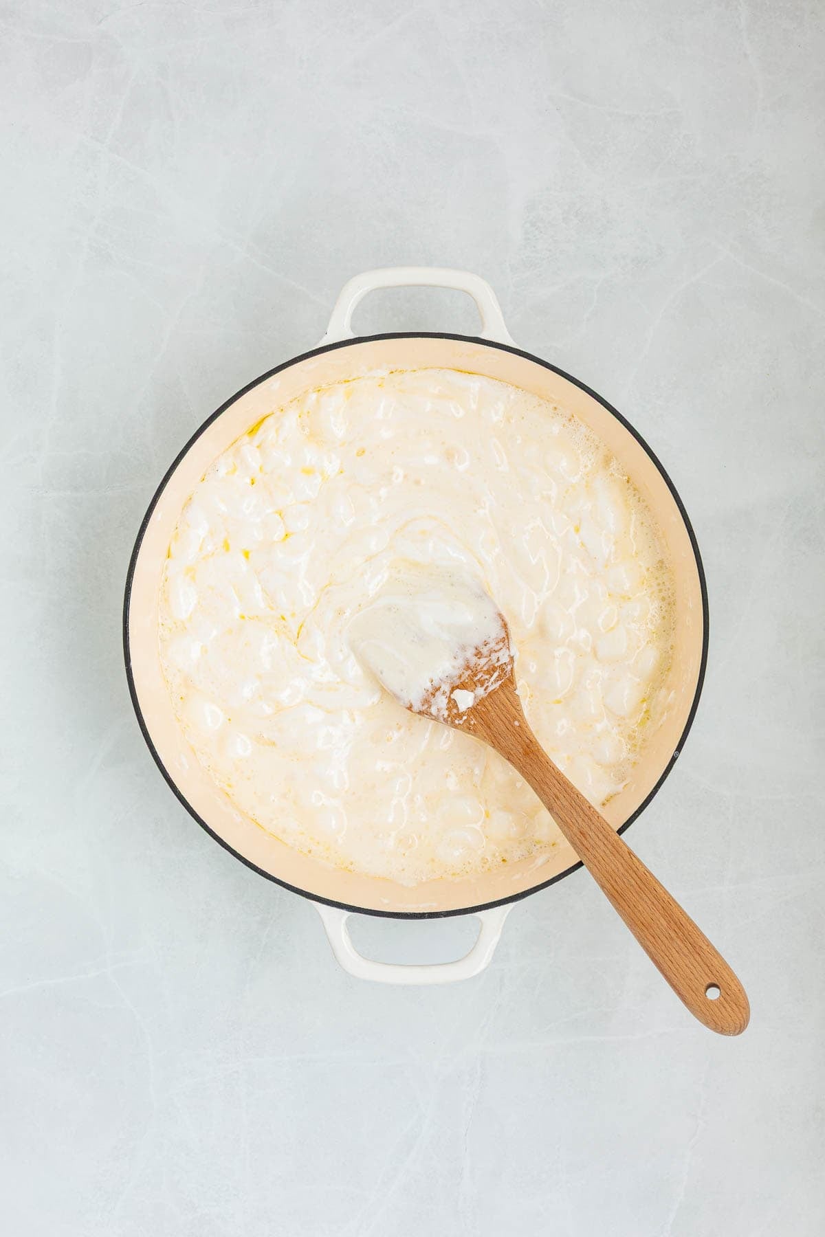 A pot filled with melted marshmallows and butter being stirred with a wooden spatula, forming the gooey base of the Rice Krispie treat mixture.