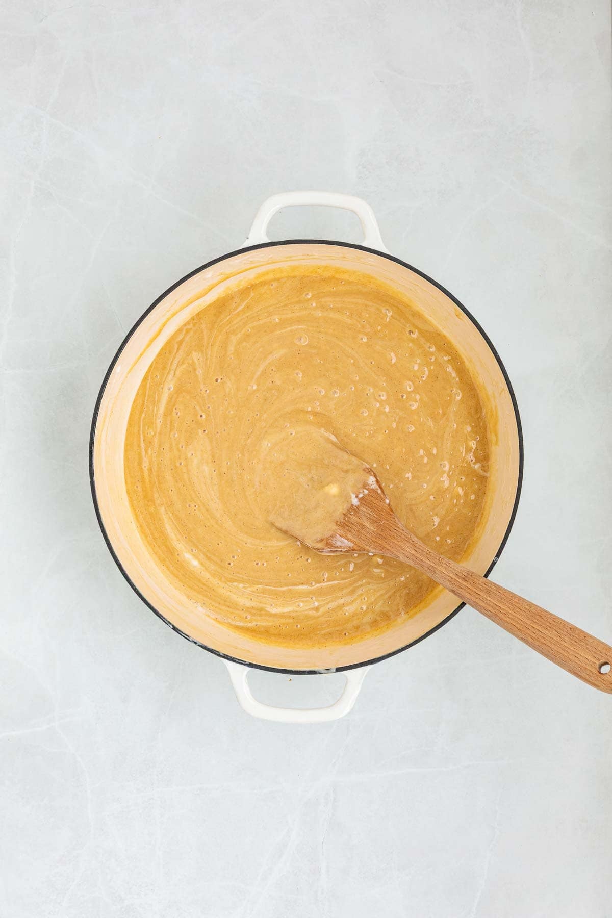 Creamy peanut butter mixed into the melted marshmallow mixture inside a pot, stirred with a wooden spatula.