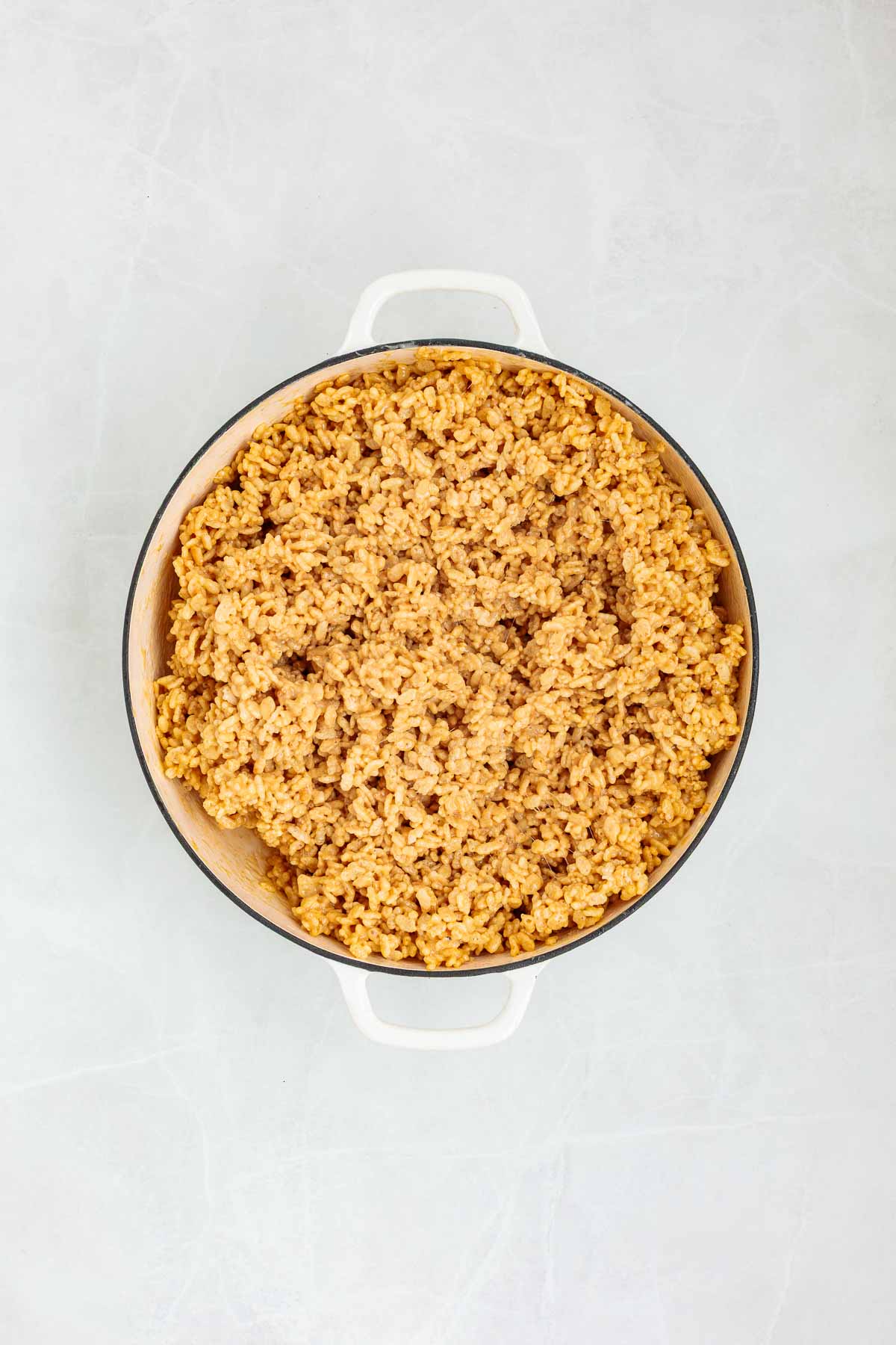 Crispy rice cereal fully mixed into the melted peanut butter-marshmallow base, forming a thick and sticky mixture in a large pot.