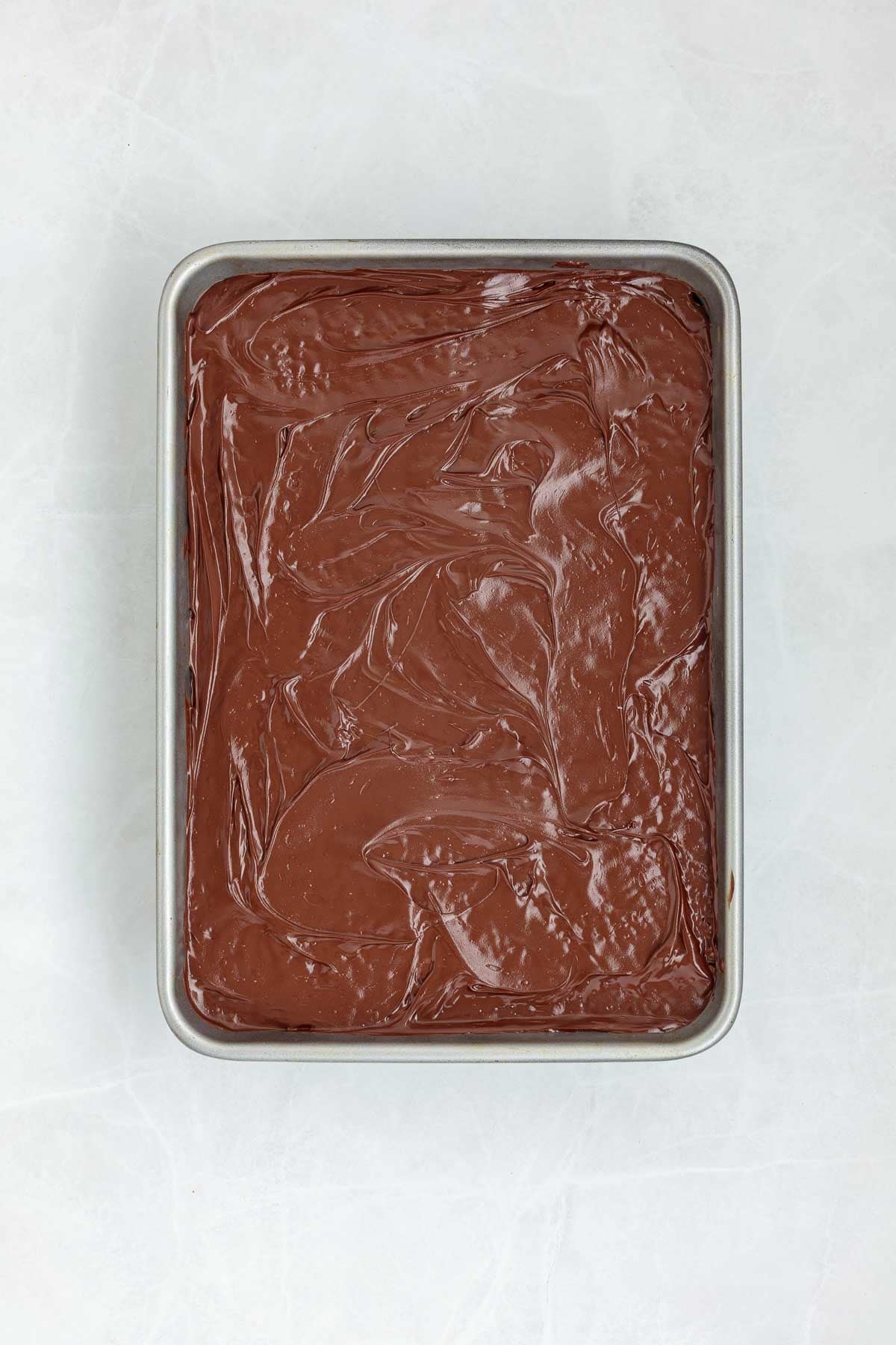 Top view of a baking tray with a smooth layer of melted chocolate spread over the Rice Krispie treat base.