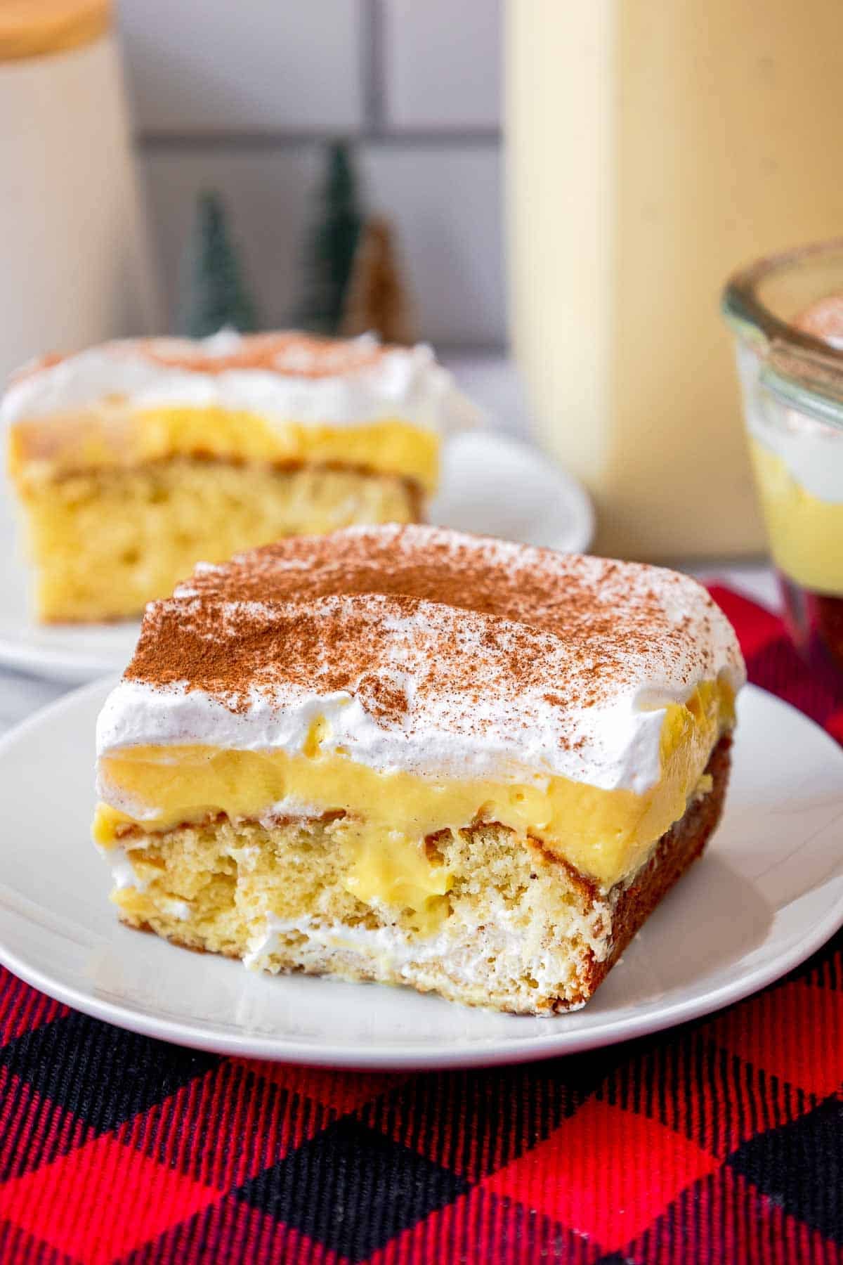 Slice of eggnog poke cake on a small plate showing butter cake layer, eggnog pudding layer, and whipped topping layer.