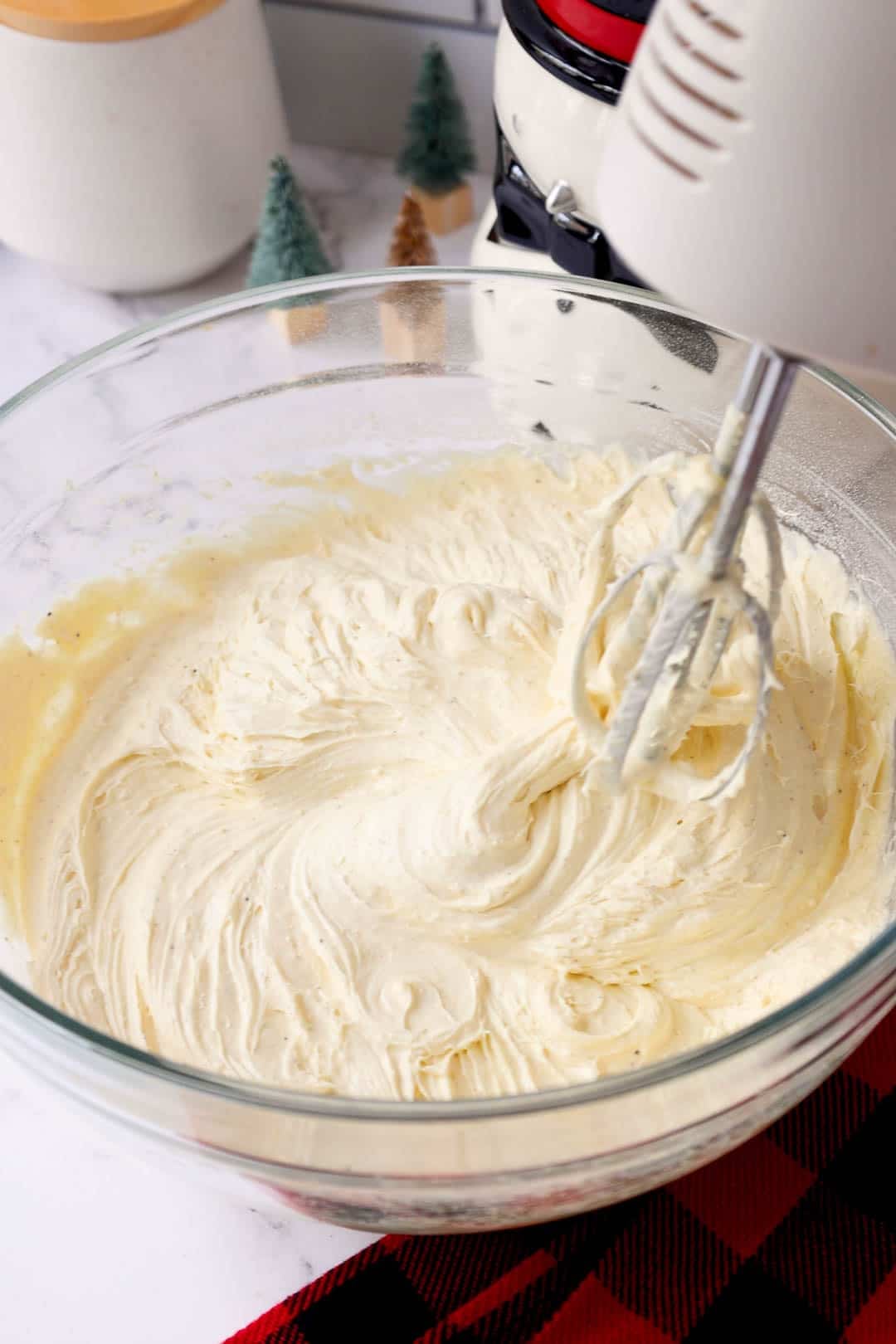 A mixing bowl of whipped eggnog butter cake mixture with electric beaters resting on the edge, ready to be added to the cake.