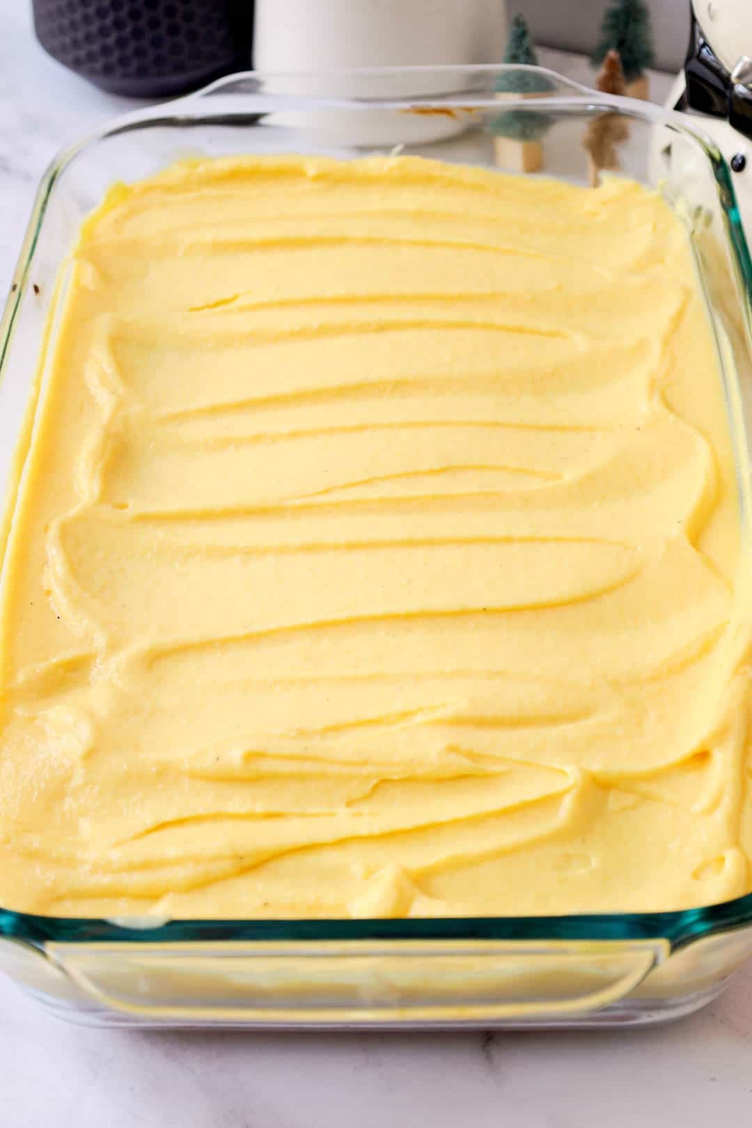 The glass baking dish filled with an even layer of eggnog pudding spread over the poked butter cake layer.