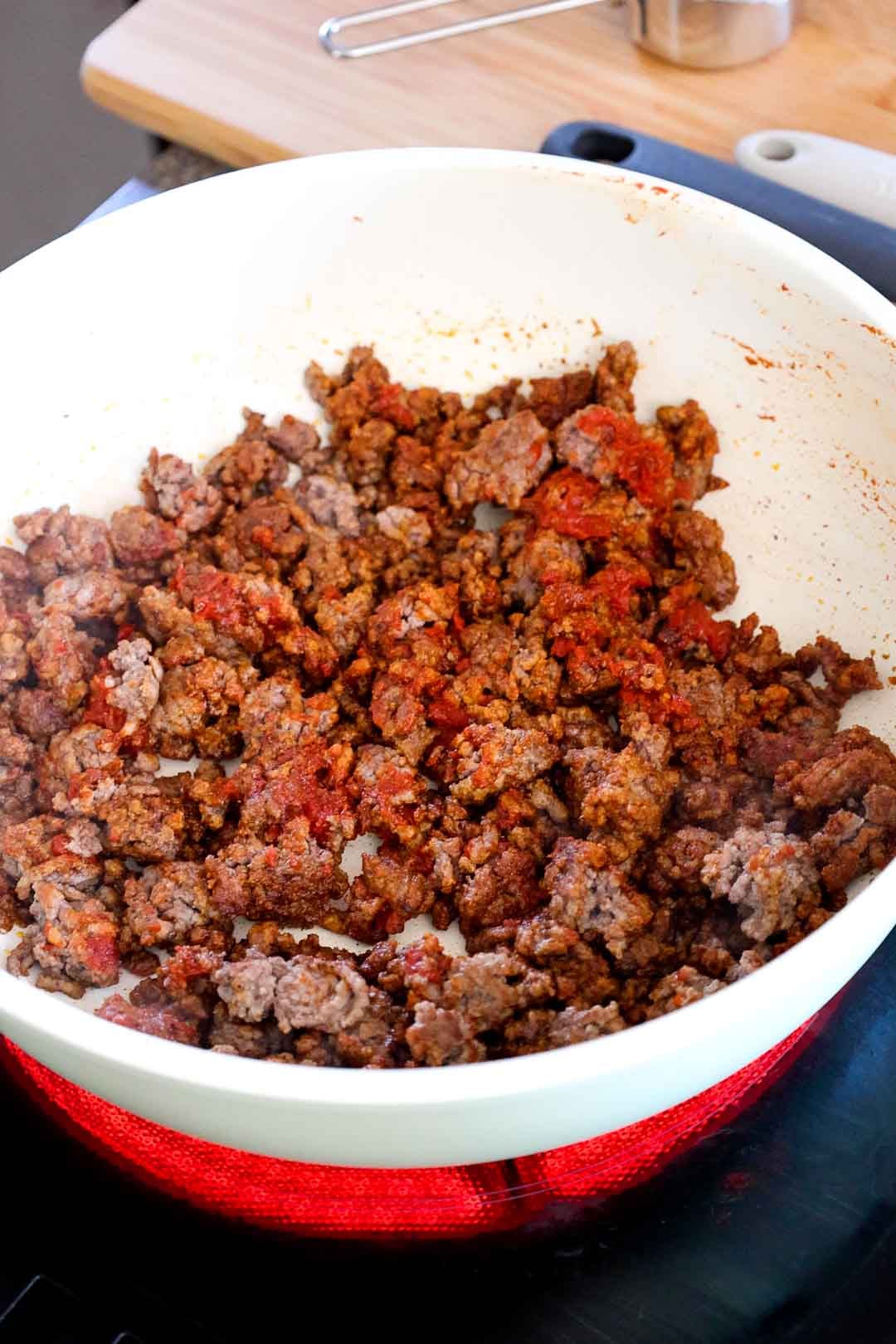 Seasoned ground beef cooking in a skillet with visible tomato paste mixed in.