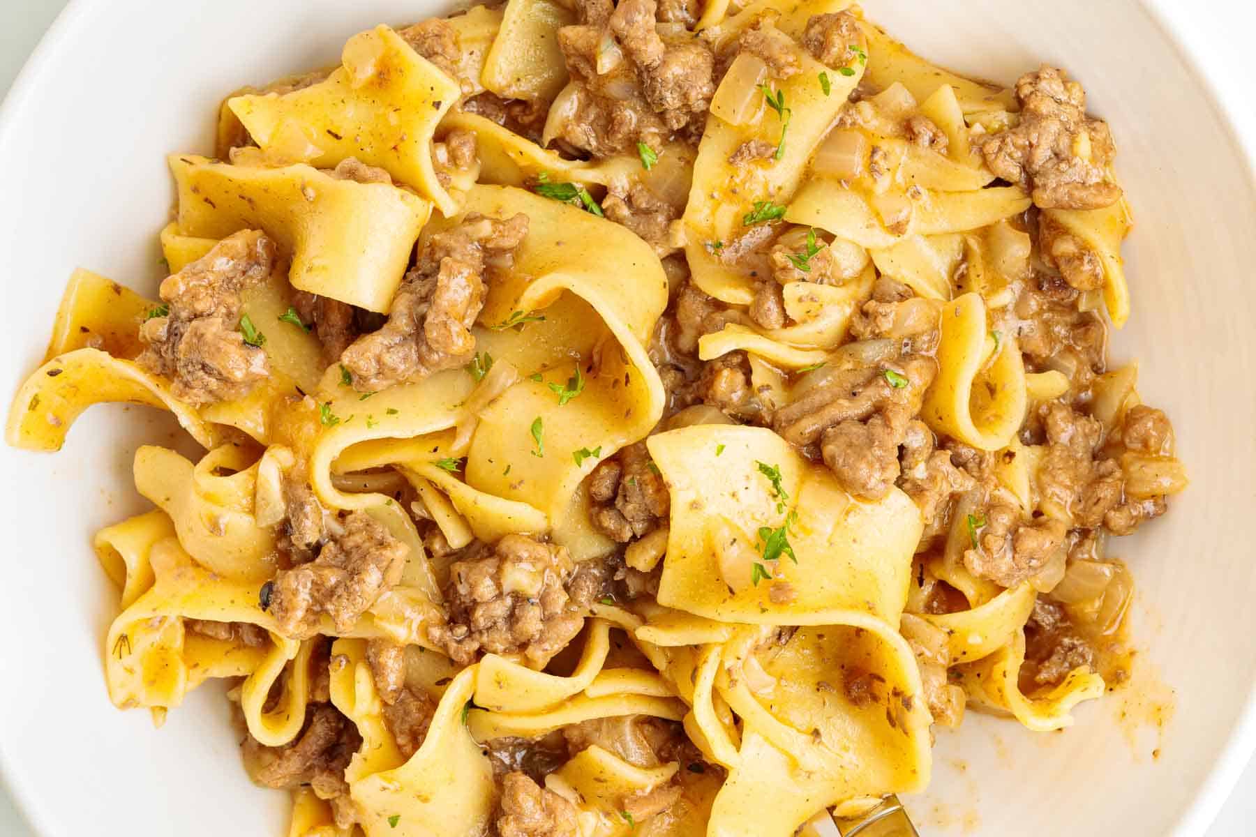 Plated ground beef egg noodles shown from above with wide egg noodles mixed with browned beef and onions. The dish looks glossy and evenly coated with sauce.