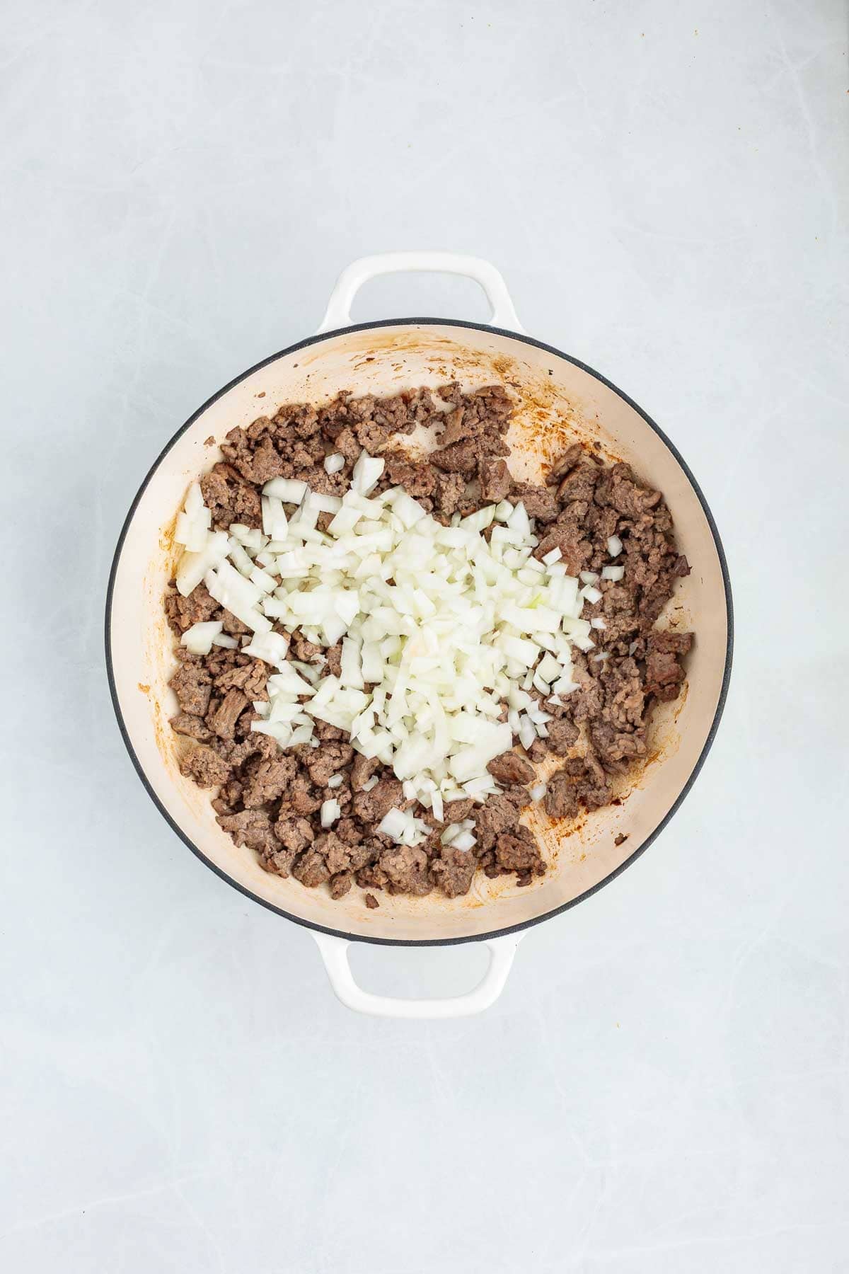 Overhead view of browned ground beef in a Dutch oven topped with chopped white onions.