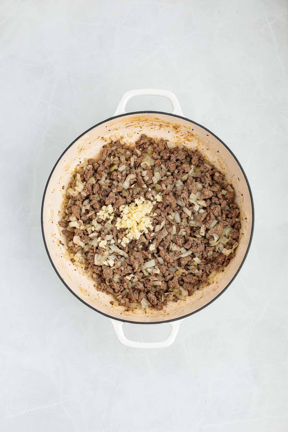 Cooked ground beef and onions in a Dutch oven with minced garlic added on top.