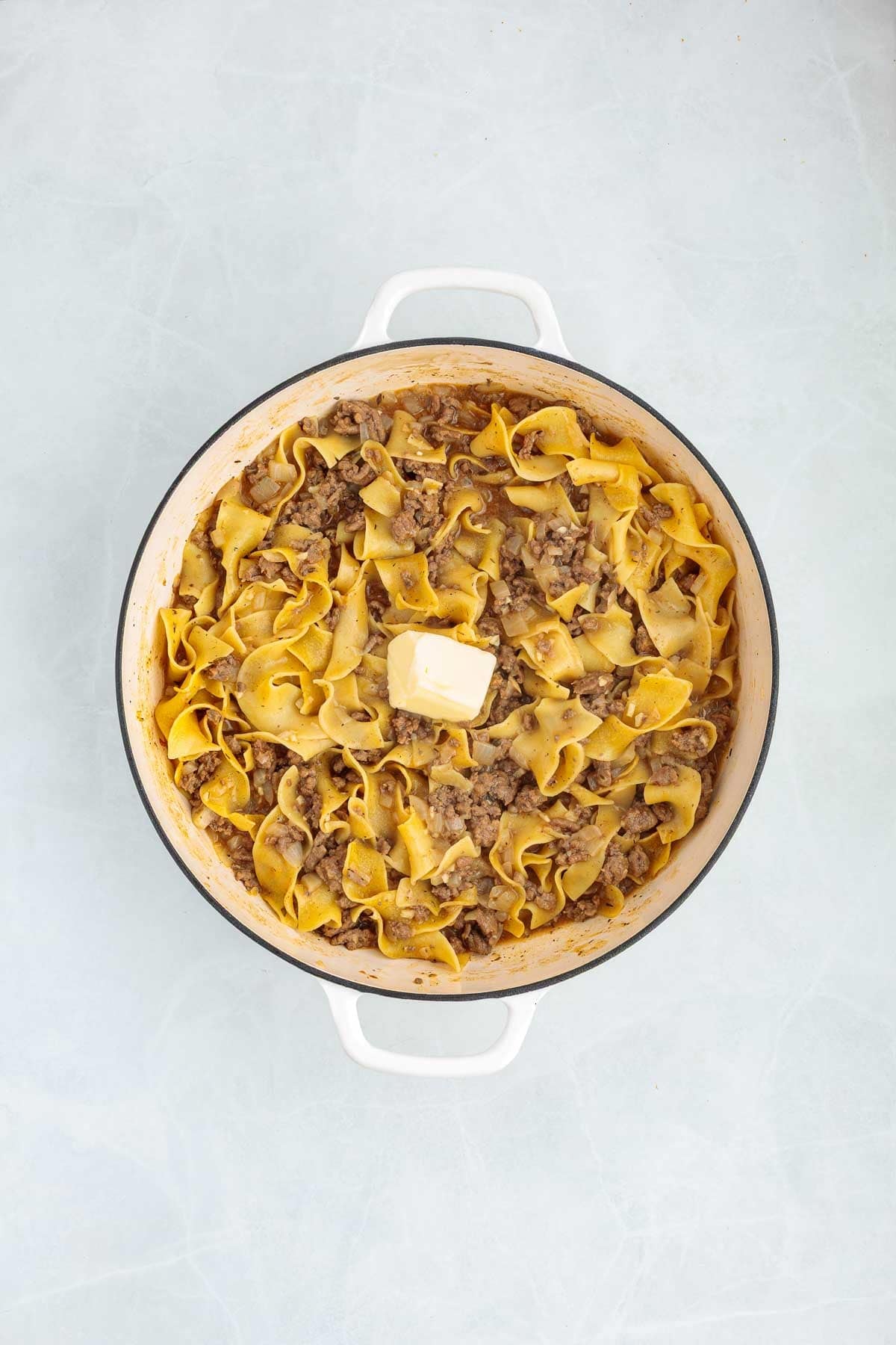 Butter melting on top of hot ground beef egg noodles in a Dutch oven.