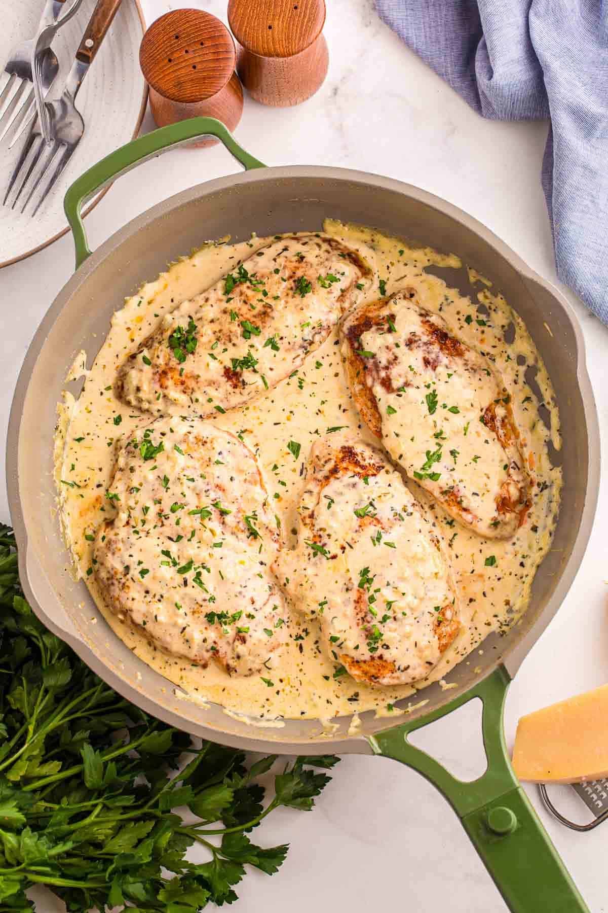 Overhead view of four chicken breasts in a skillet with creamy garlic sauce and parsley on top.