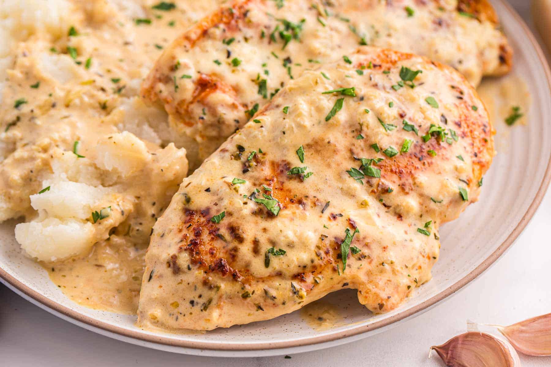 Chicken breasts covered in creamy garlic sauce plated with mashed potatoes.