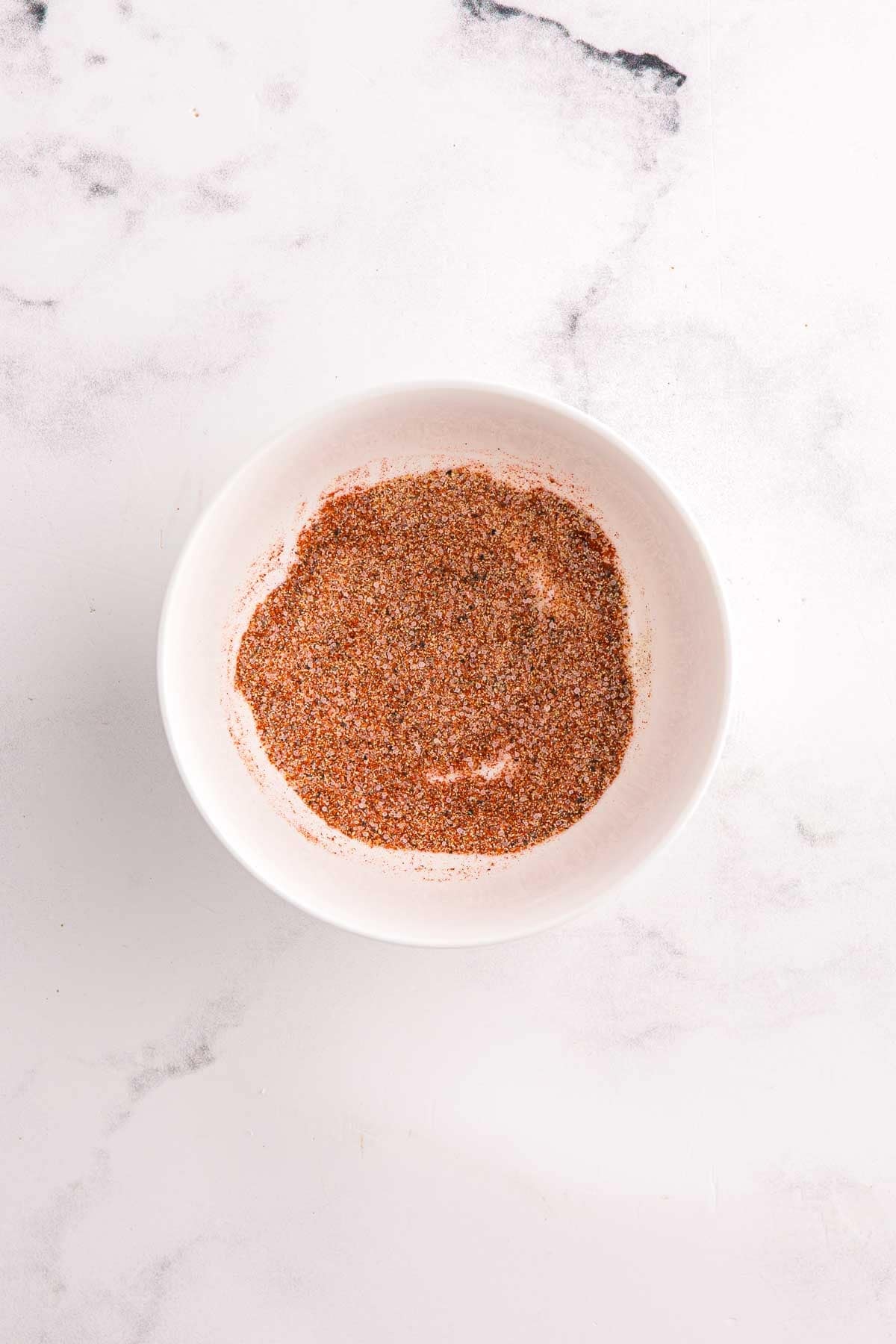 Small bowl of mixed spices on a marble surface. Seasoning blend for creamy garlic chicken.