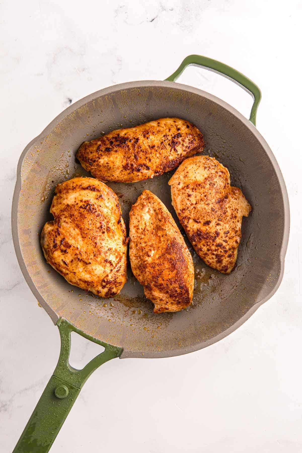 Four seasoned chicken breasts searing in a skillet until browned. First step in making creamy garlic chicken.