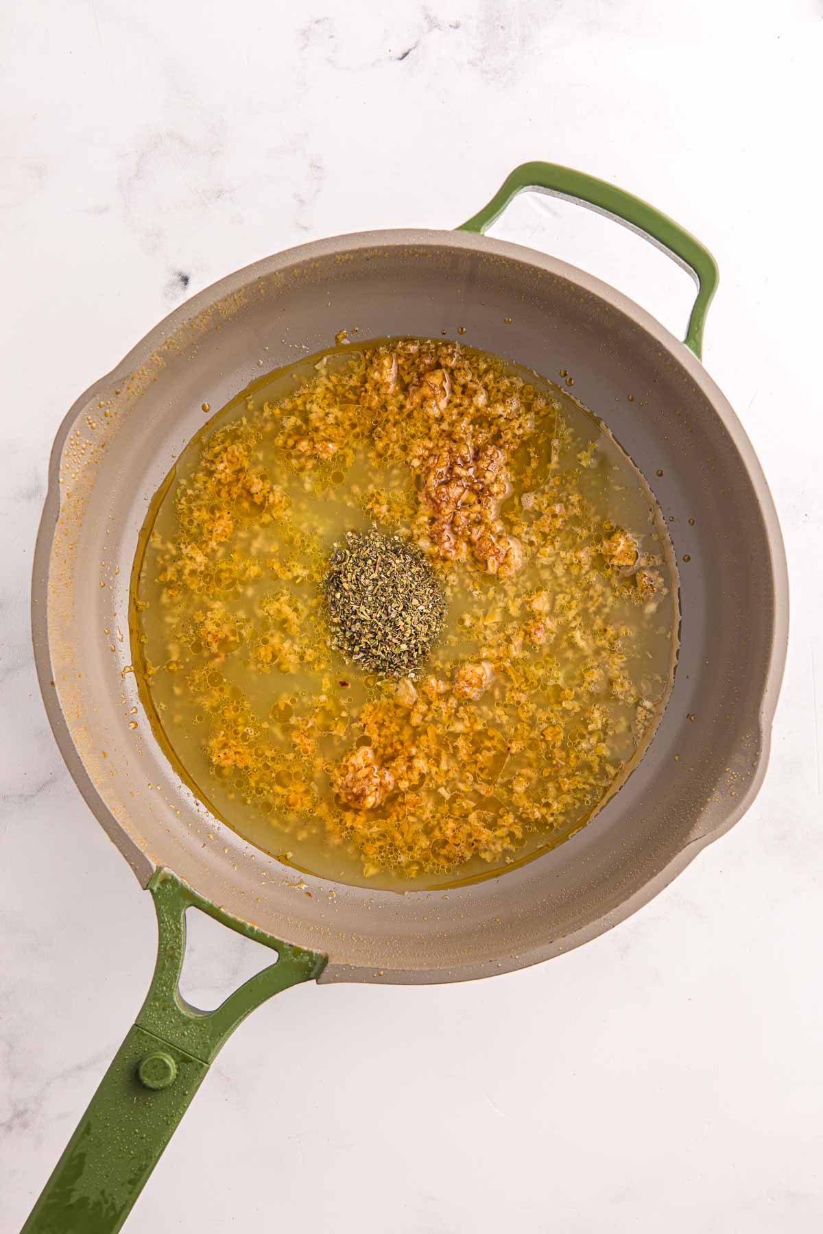 Chicken broth and herbs added to garlic in a skillet. Sauce simmering for creamy garlic chicken.