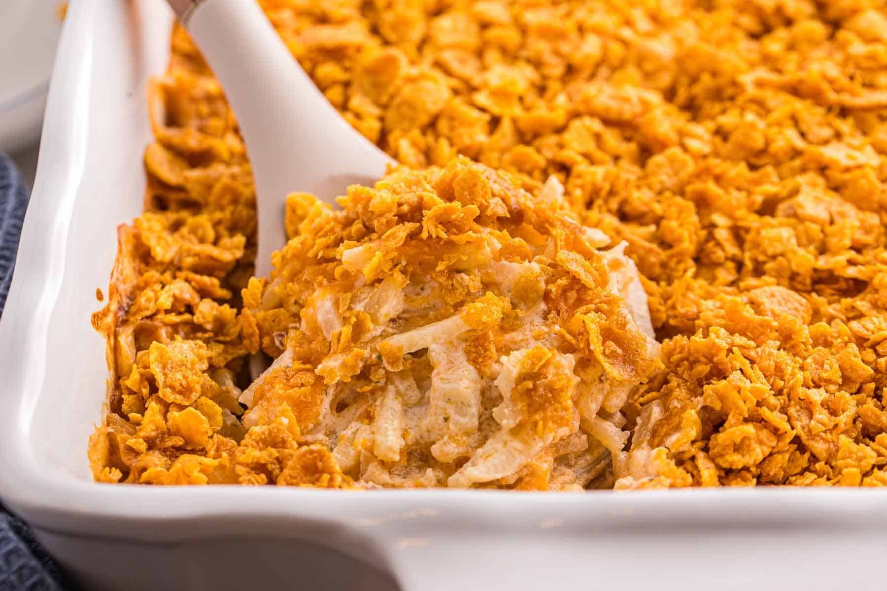 Spoon scooping a portion of baked hash brown casserole from a baking dish, showing the creamy interior and crisp golden topping.