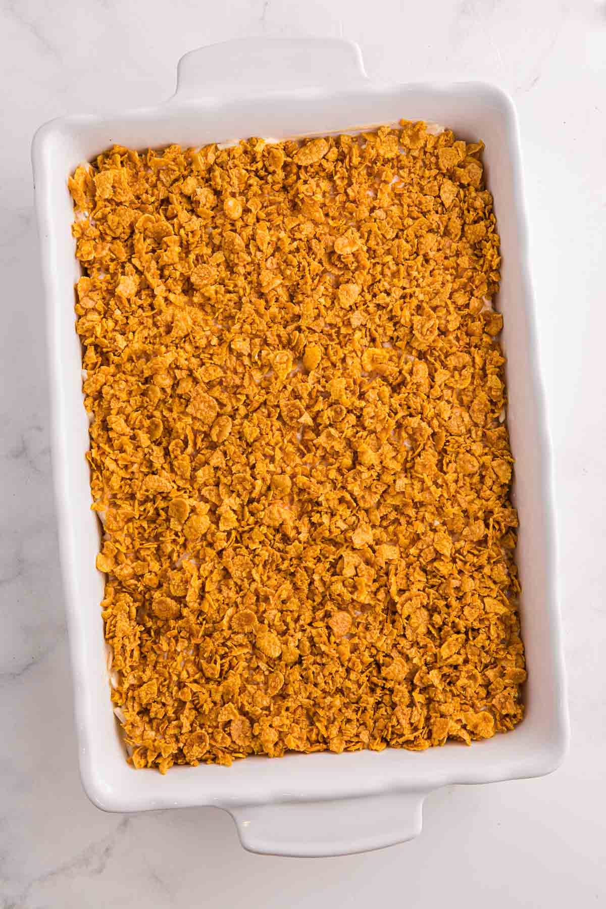 Baking dish topped with a thick layer of crushed cornflakes covering the hash brown casserole evenly before baking.