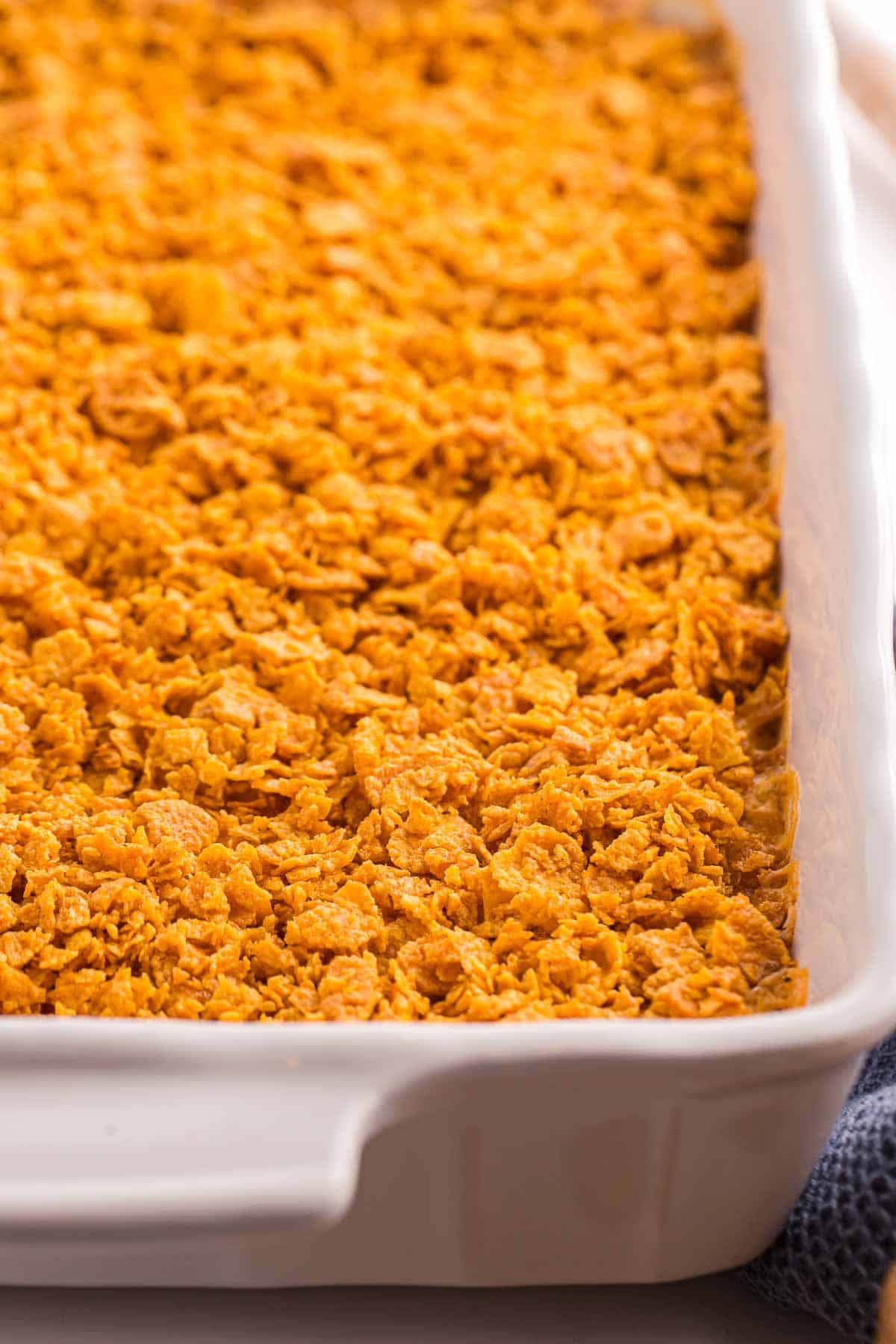 Close up of baked hash brown casserole in a white dish with a crispy golden cornflake topping. The surface looks crunchy and evenly browned across the pan.