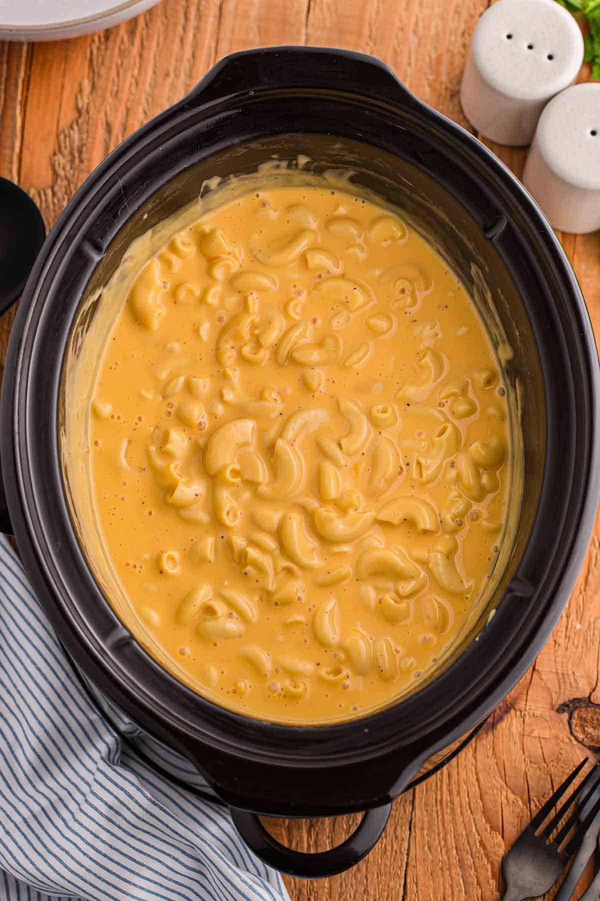 Overhead view of crockpot mac and cheese fully cooked in a slow cooker. The elbow macaroni is evenly coated in a thick and creamy cheese sauce.