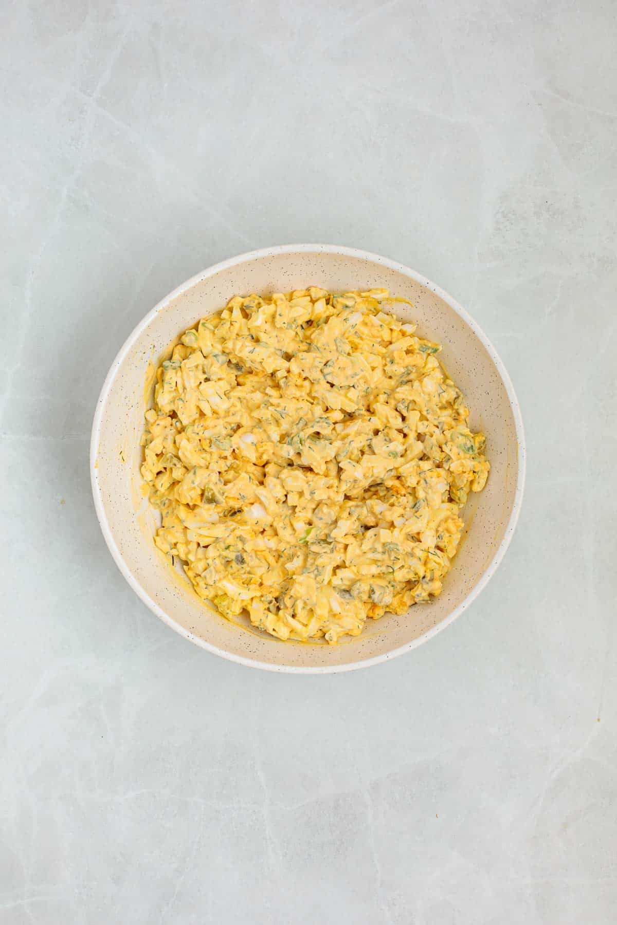 Finished dill pickle egg salad in a bowl with chopped eggs, pickles, and fresh dill fully mixed into a creamy texture.