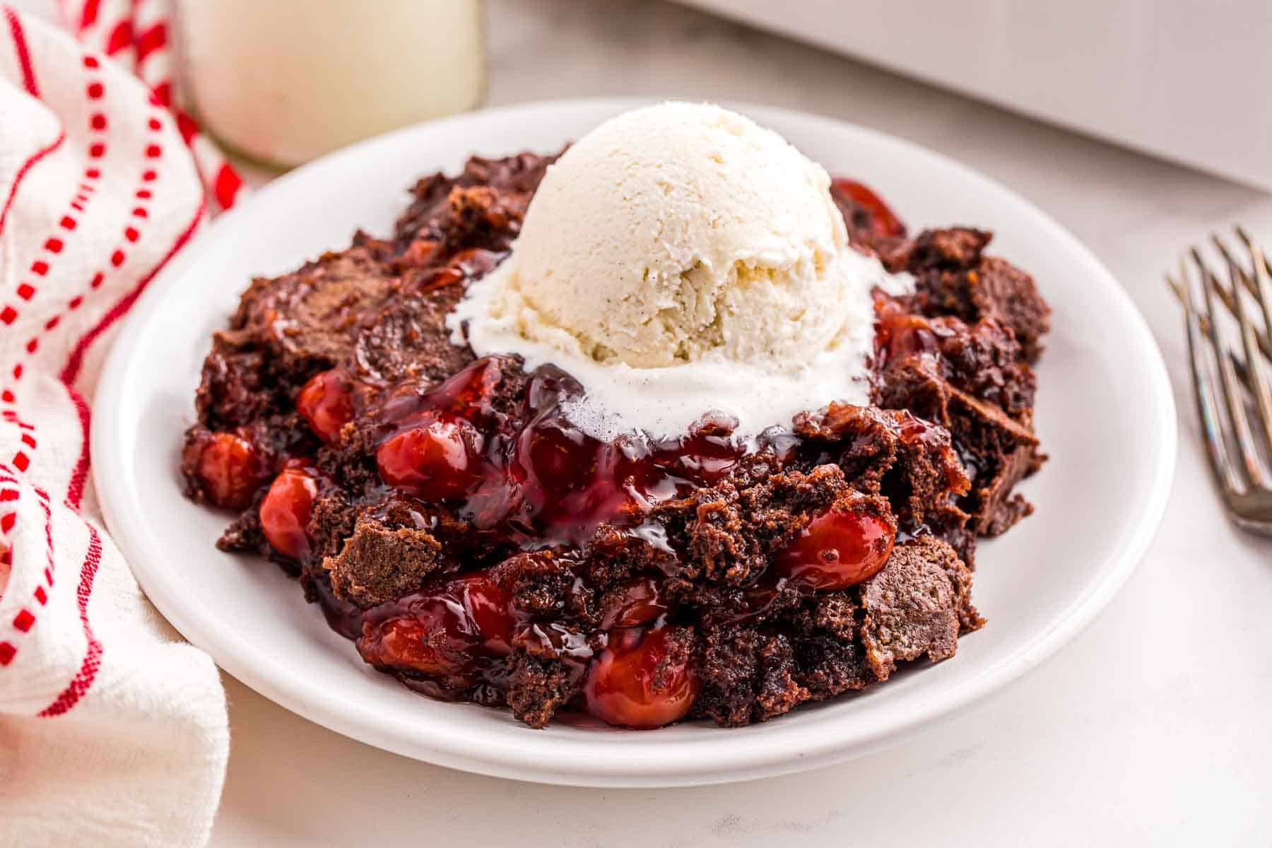 Serving of cherry dump cake with vanilla ice cream on a plate.