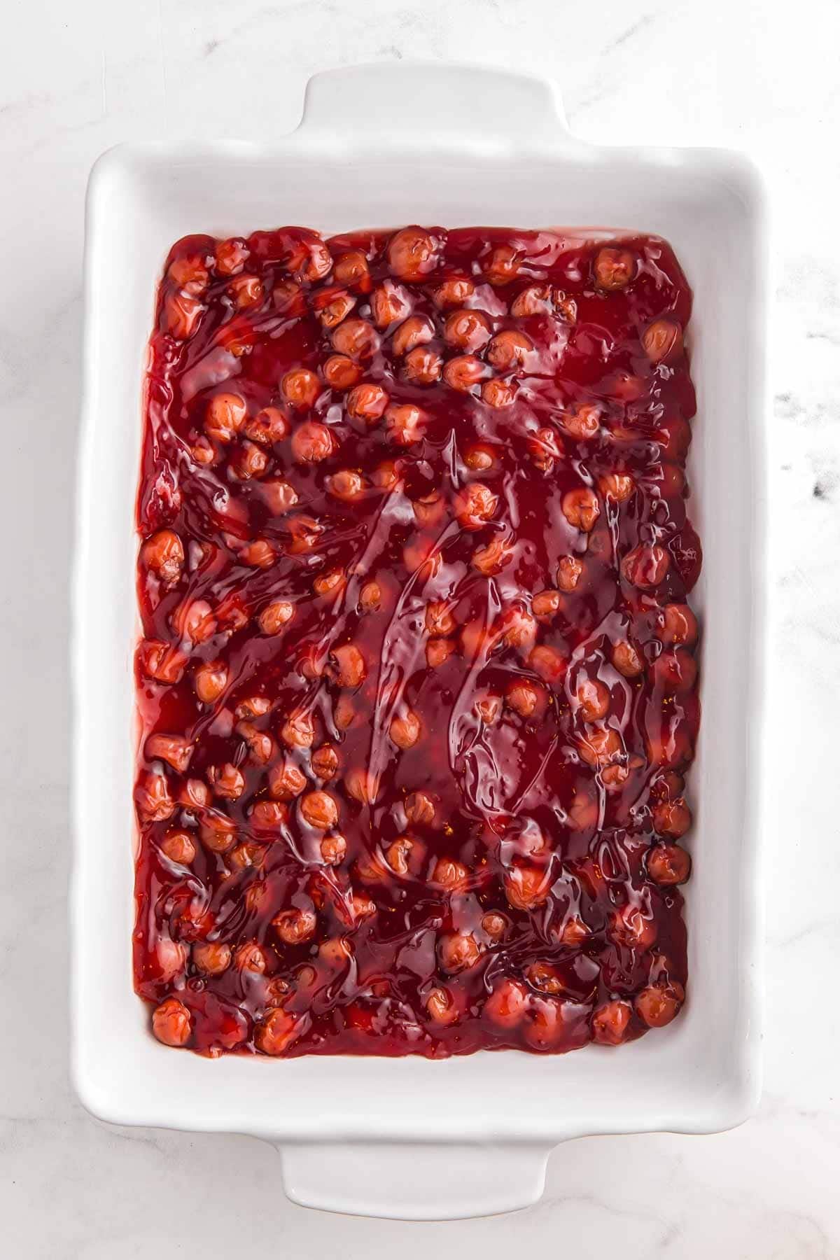 Cherry pie filling spread in an even layer in a white 9 by 13 inch baking dish.