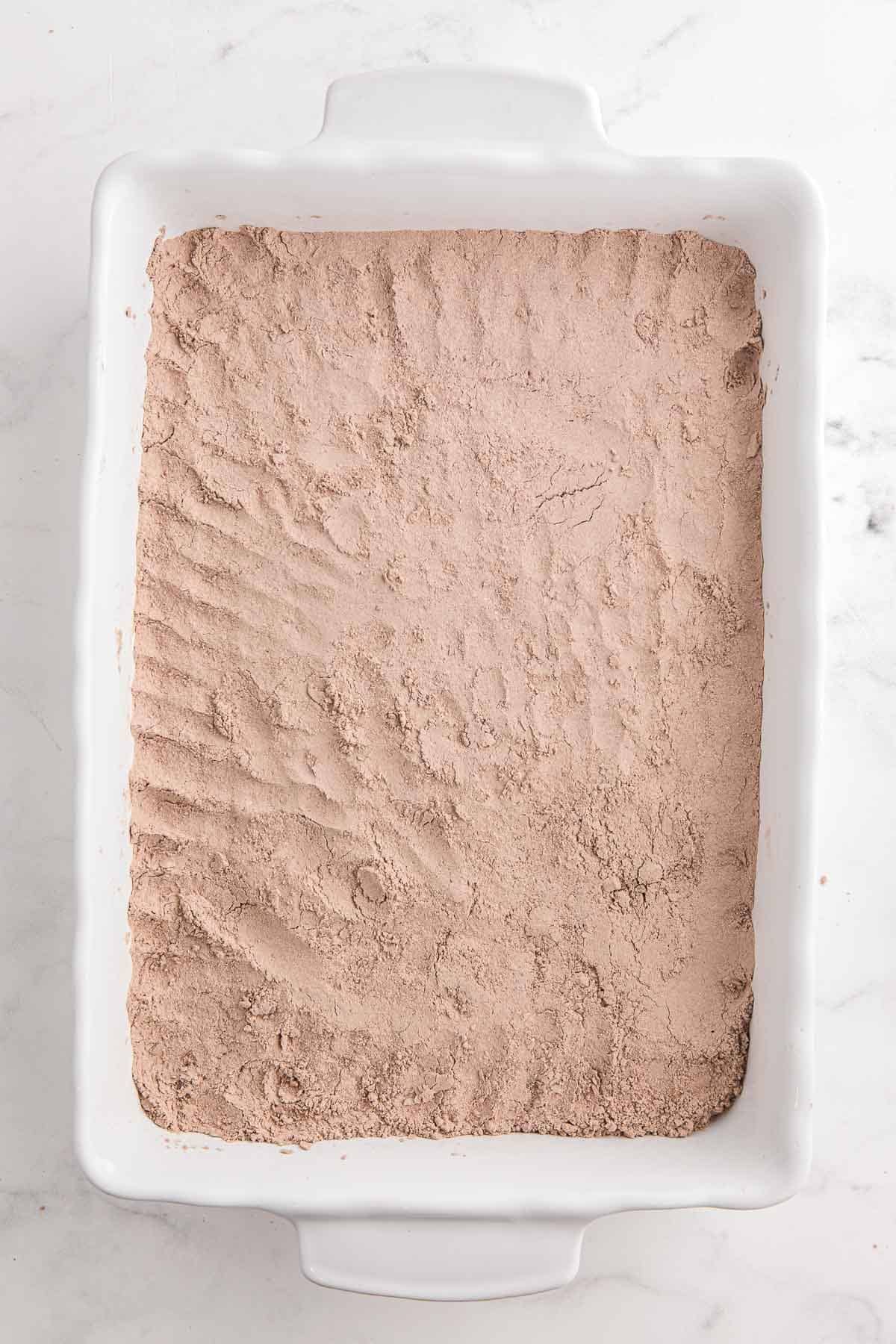 Dry chocolate cake mix spread evenly over cherry filling in a white 9 by 13 inch baking dish.