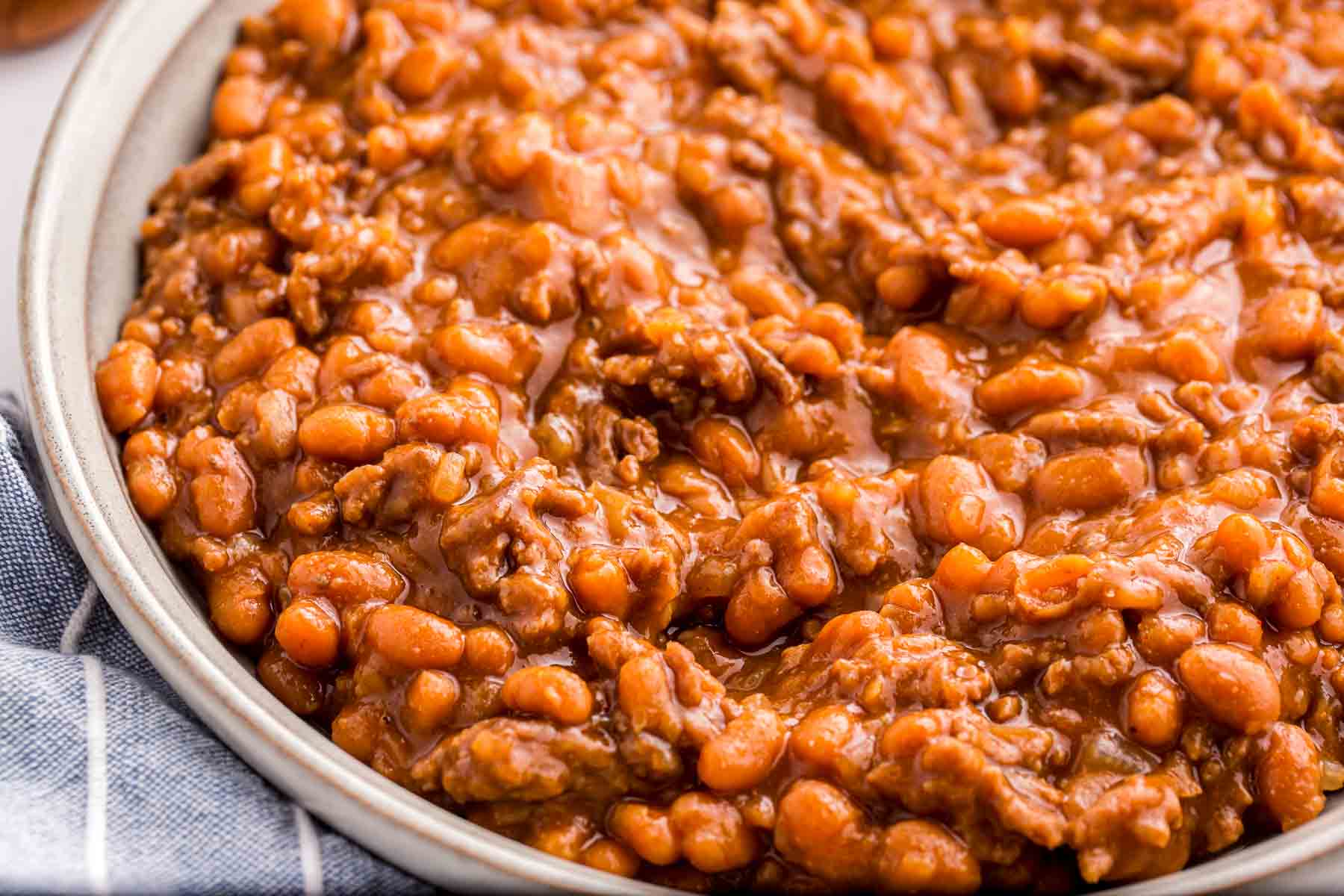 Close up of baked beans with ground beef served in a shallow bowl. The thick sauce coats the beans and beef, giving the dish a rich and hearty appearance.