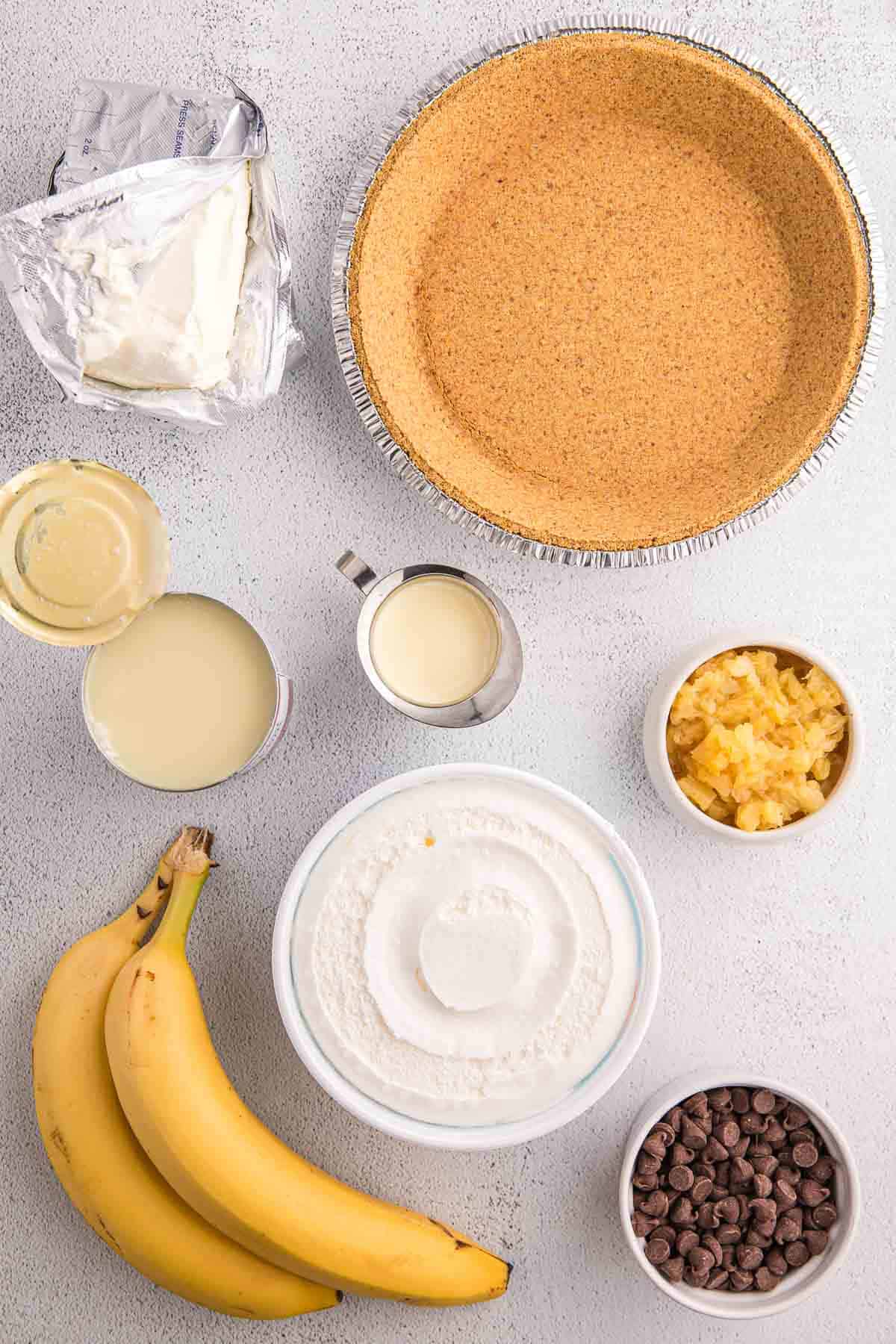 Ingredients for no bake banana split pie including bananas, cream cheese, crushed pineapple, sweetened condensed milk, chocolate chips, and a graham cracker crust.