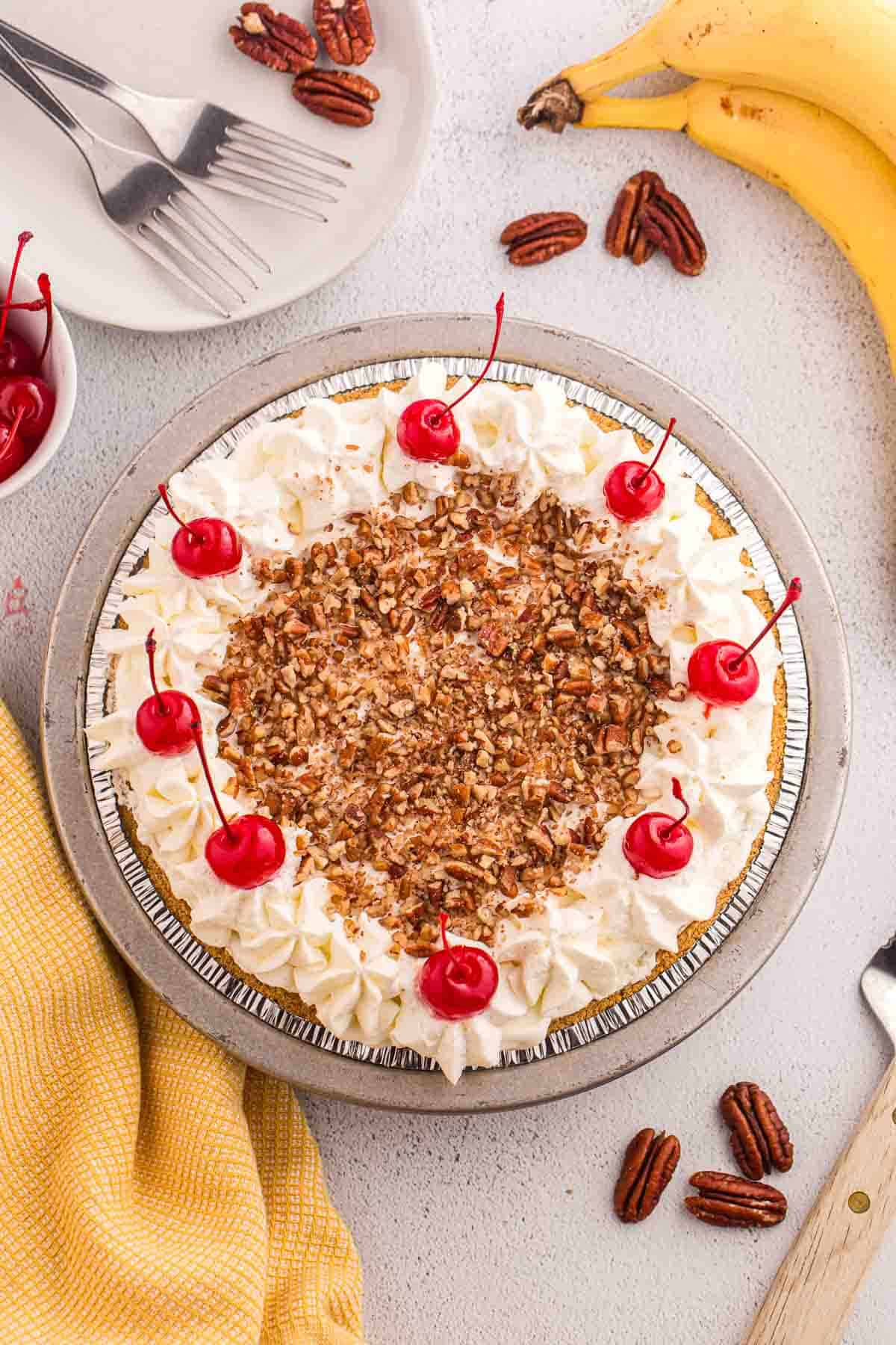 Overhead view of finished no bake banana split pie topped with whipped cream, chopped pecans, and cherries.