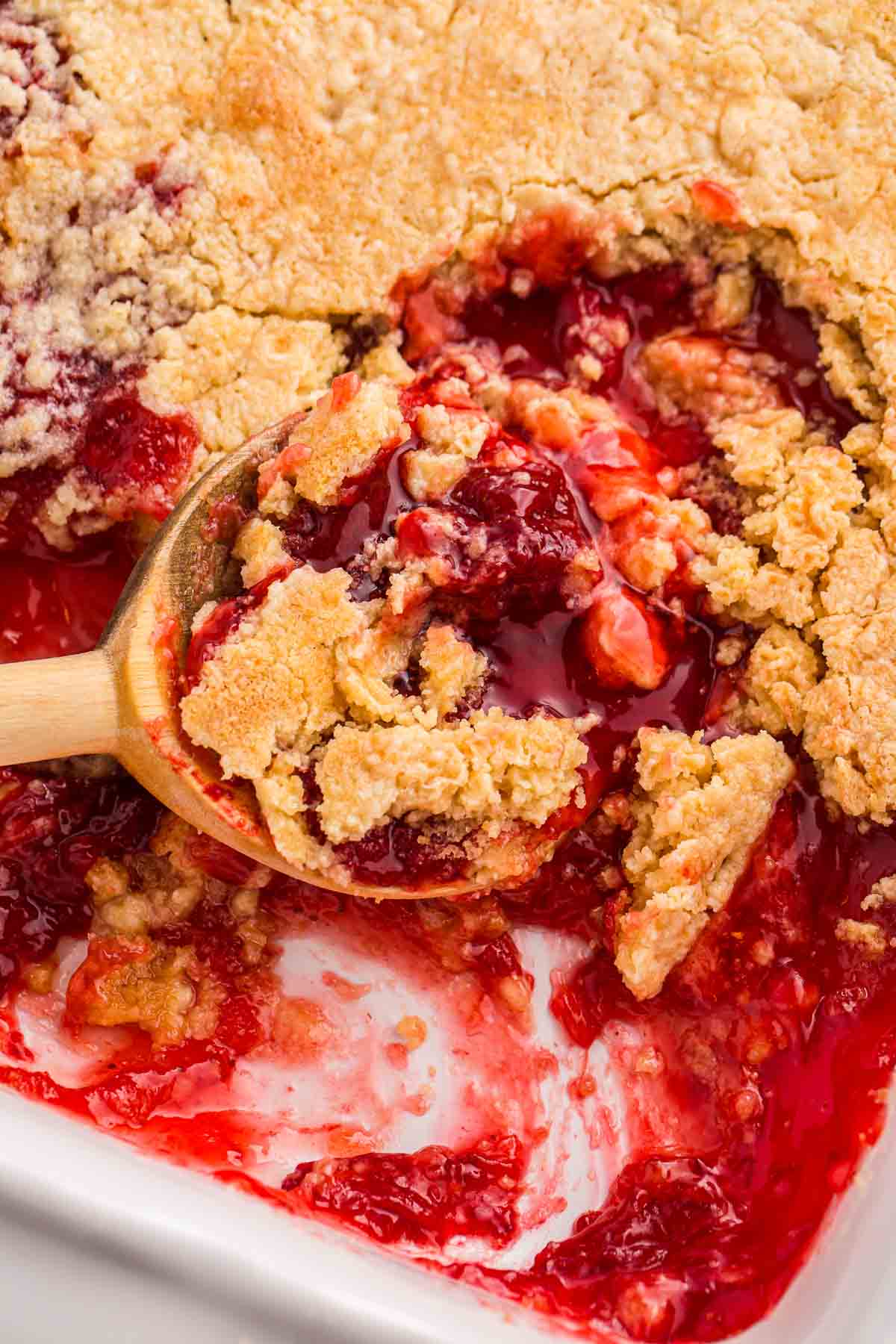 Spoon scooping strawberry dump cake with golden cake topping and strawberry filling from a baking dish.