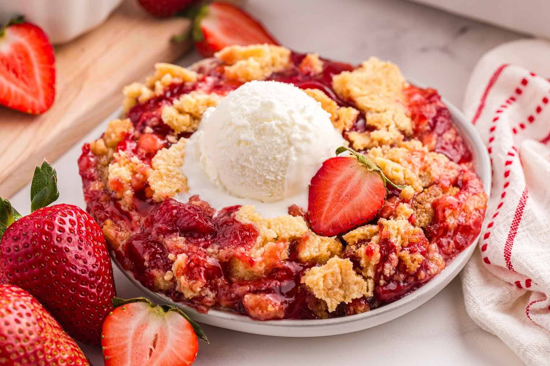 Strawberry dump cake with vanilla ice cream served on a plate beside fresh strawberries.