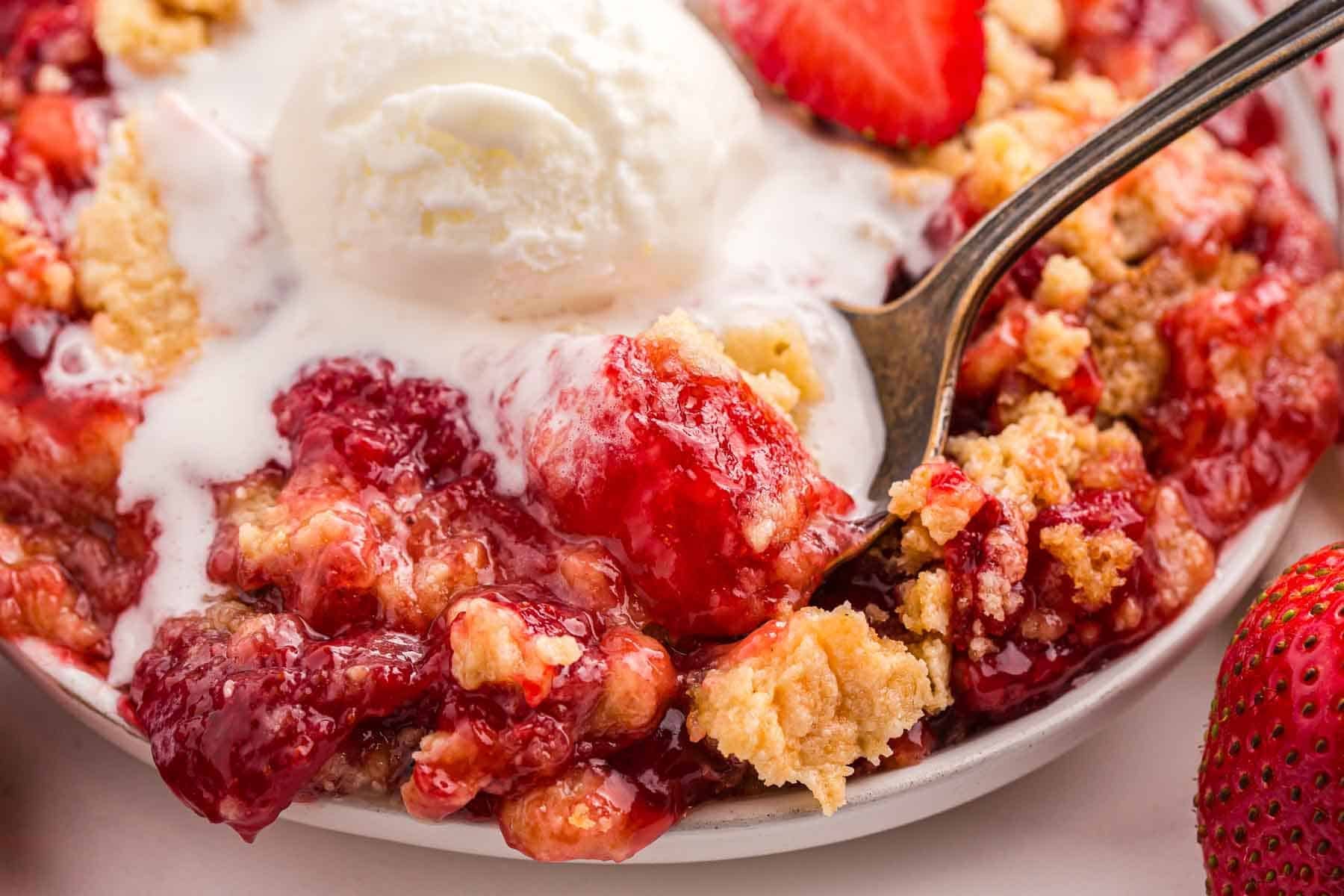 Spoonful of strawberry dump cake with melting vanilla ice cream and strawberry filling.