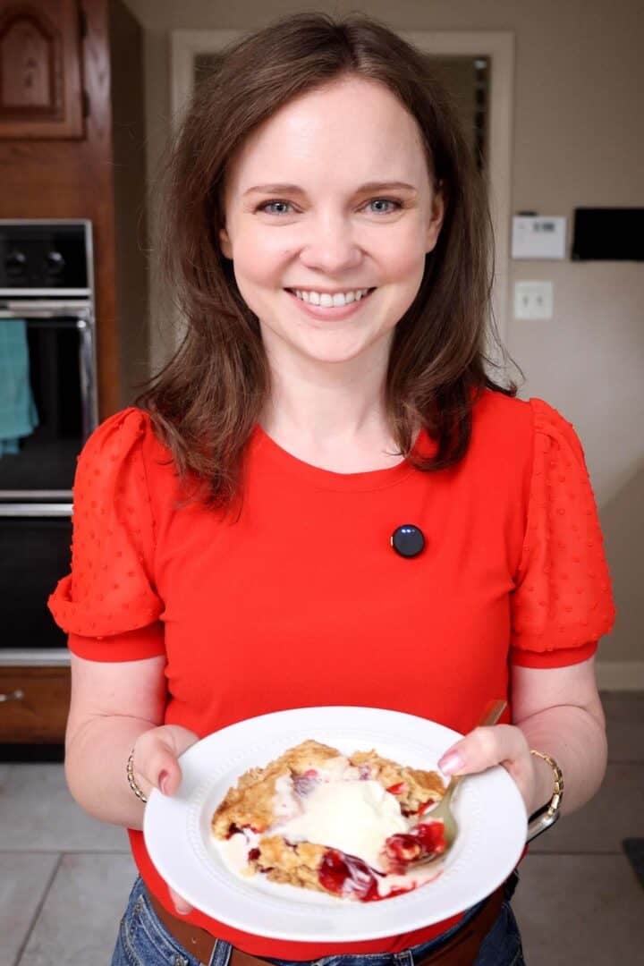 Kelsey Smith holding a plate of strawberry dump cake topped with melting vanilla ice cream.