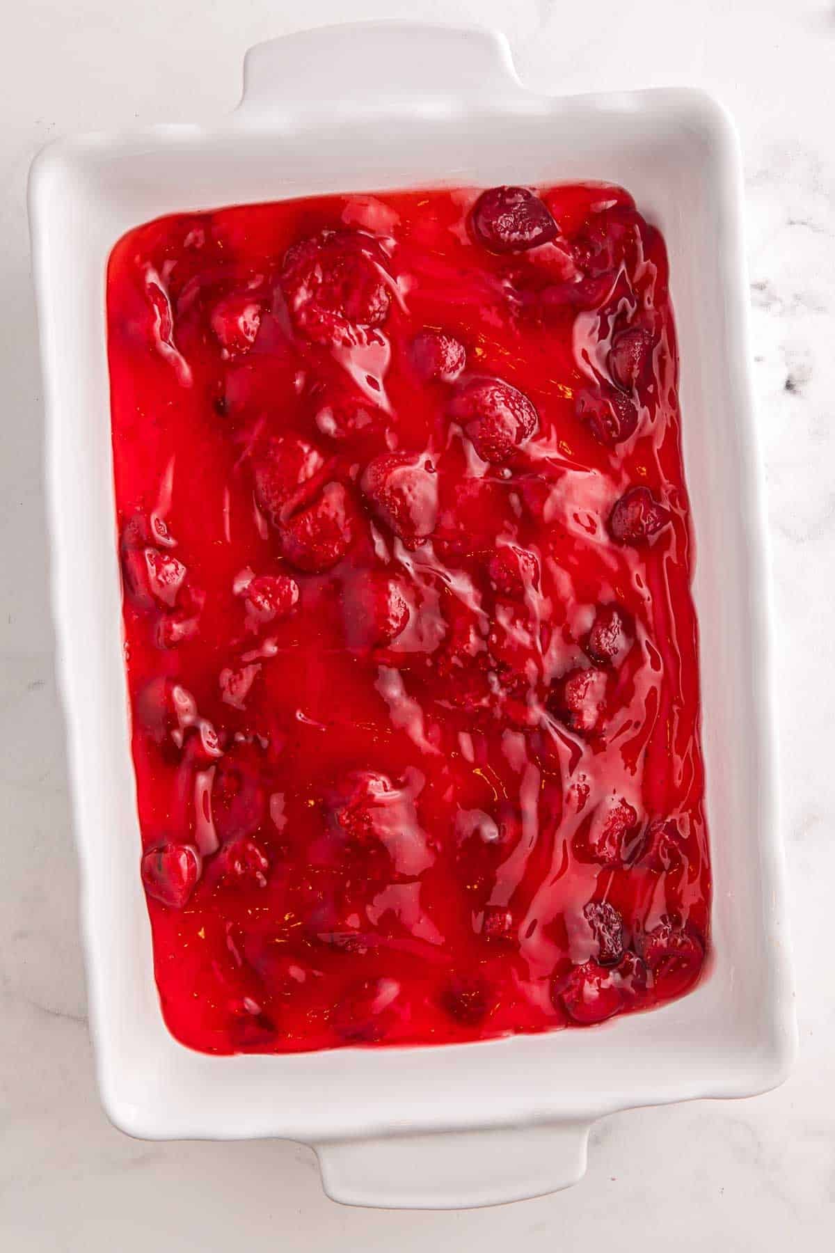 Strawberry pie filling spread in a 9 by 13 inch white baking dish before adding cake mix.