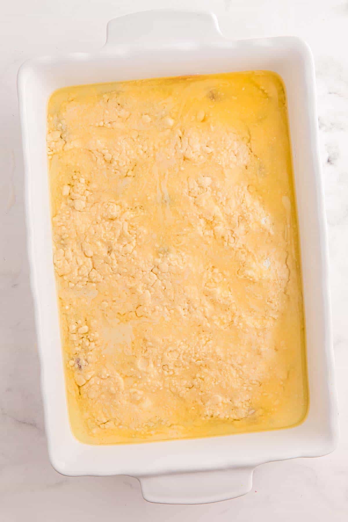 Melted butter poured over cake mix in a baking dish before baking strawberry dump cake.