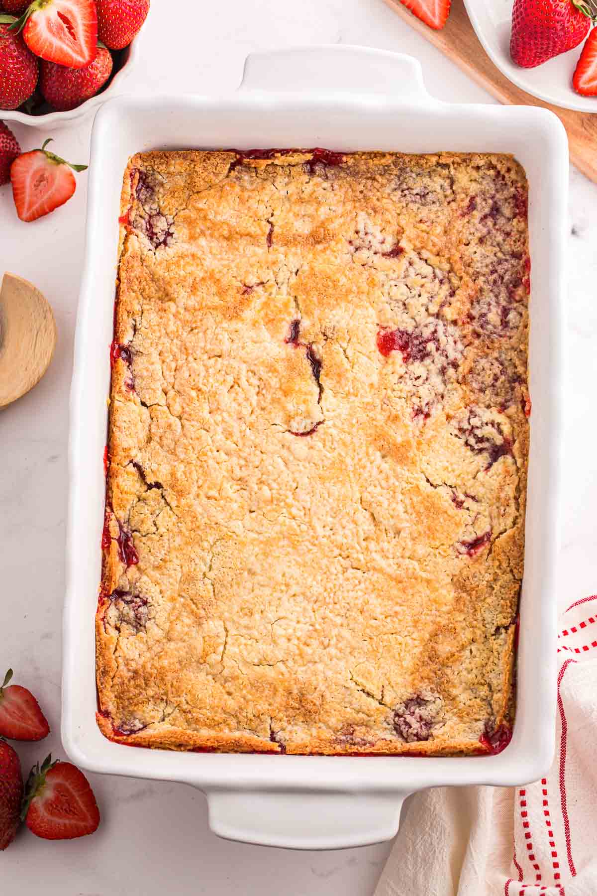 Freshly baked strawberry dump cake in a white 9 by 13 inch casserole dish with a golden brown crust and strawberry filling bubbling through the edges.