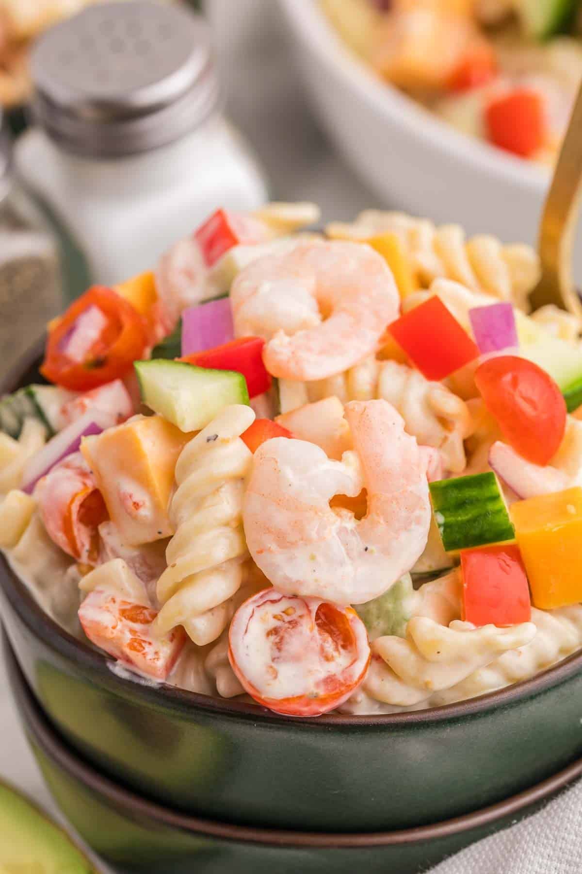Spoonful of creamy shrimp pasta salad showing rotini pasta, shrimp, cucumber, cherry tomatoes, bell pepper, red onion, and cheddar cheese.