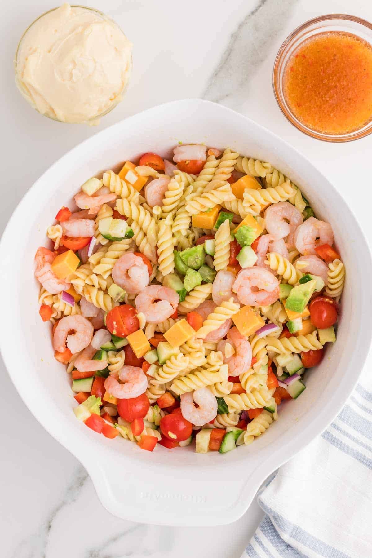 Rotini pasta mixed with shrimp, cucumber, avocado, cherry tomatoes, bell pepper, red onion, and cheddar cheese before the dressing is added.