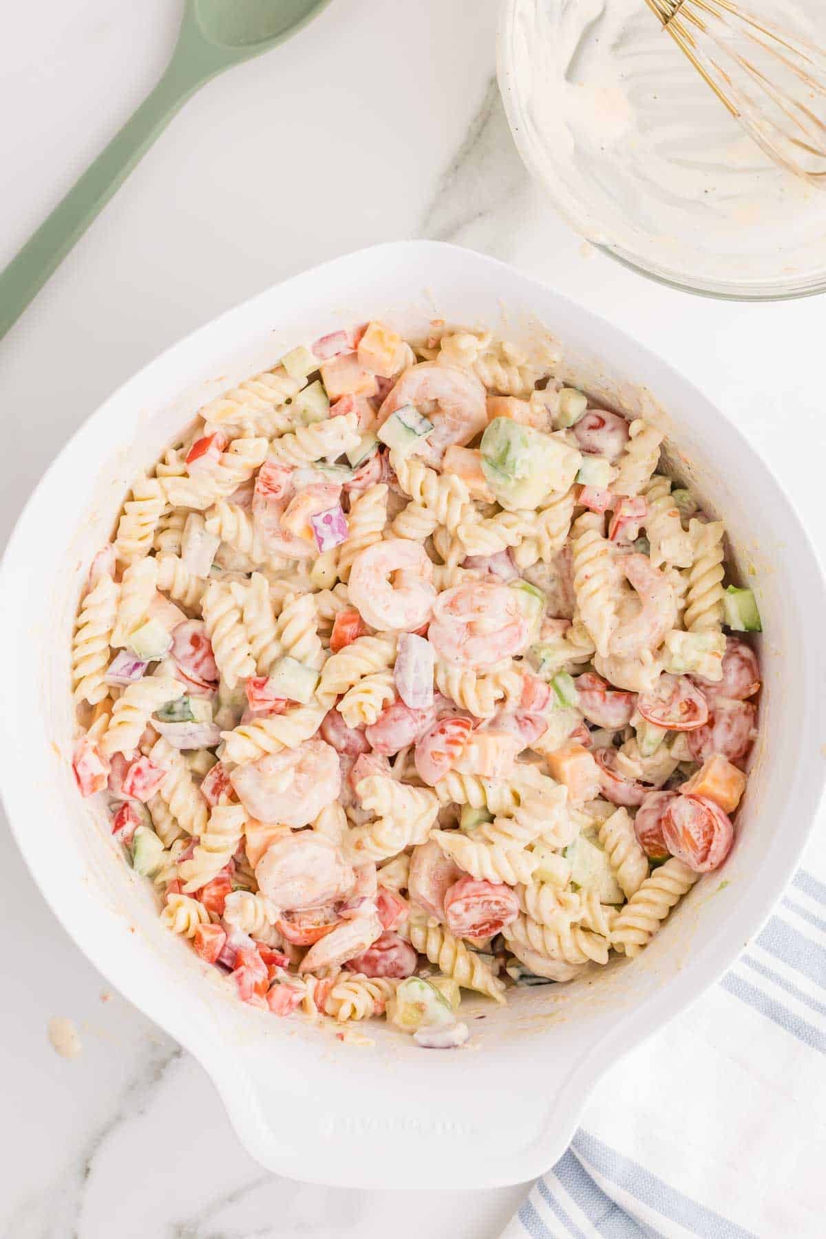 Shrimp pasta salad tossed with creamy dressing until the rotini pasta, shrimp, vegetables, avocado, and cheese are evenly coated.