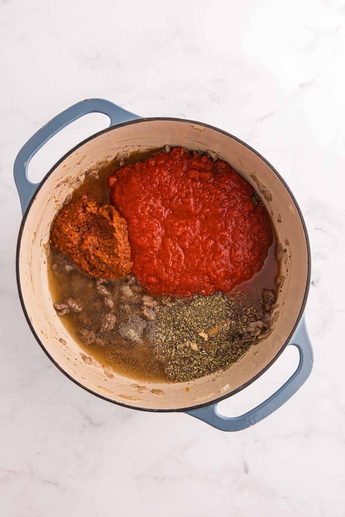 Browned ground beef and softened onion are topped with marinara sauce petite diced tomatoes beef broth and seasonings in the Dutch oven. The ingredients are ready to be stirred and brought to a gentle boil.