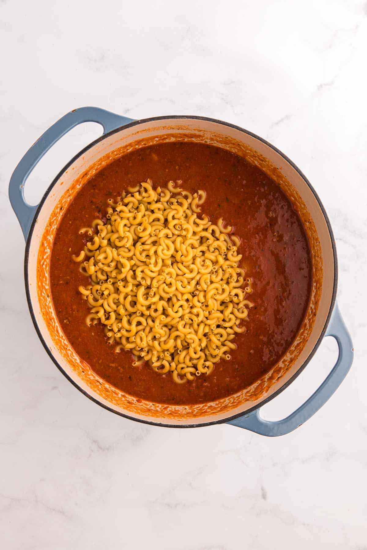 Dry elbow macaroni is added to the tomato and beef mixture in the Dutch oven. The pasta will simmer directly in the sauce until tender.
