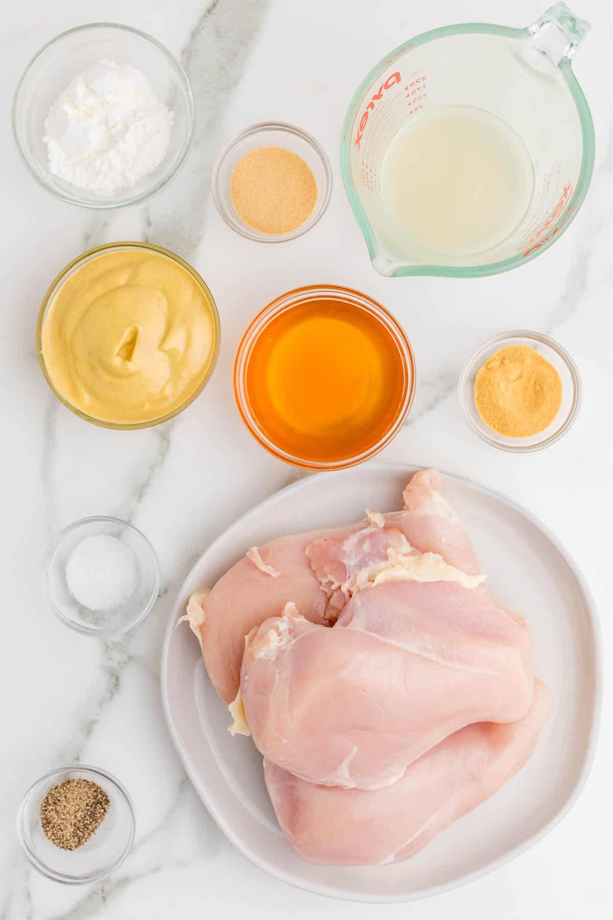 Ingredients for Slow Cooker Honey Mustard Chicken arranged on a counter, Boneless skinless chicken breasts, garlic powder, onion powder, salt, black pepper, dijon mustard, honey, chicken broth, and cornstarch.