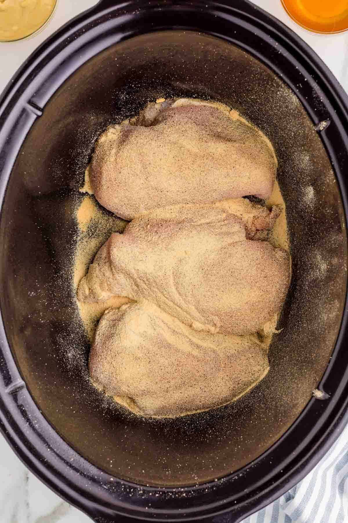 Three raw chicken breasts placed in a slow cooker and evenly covered with garlic powder, onion powder, salt, and black pepper.