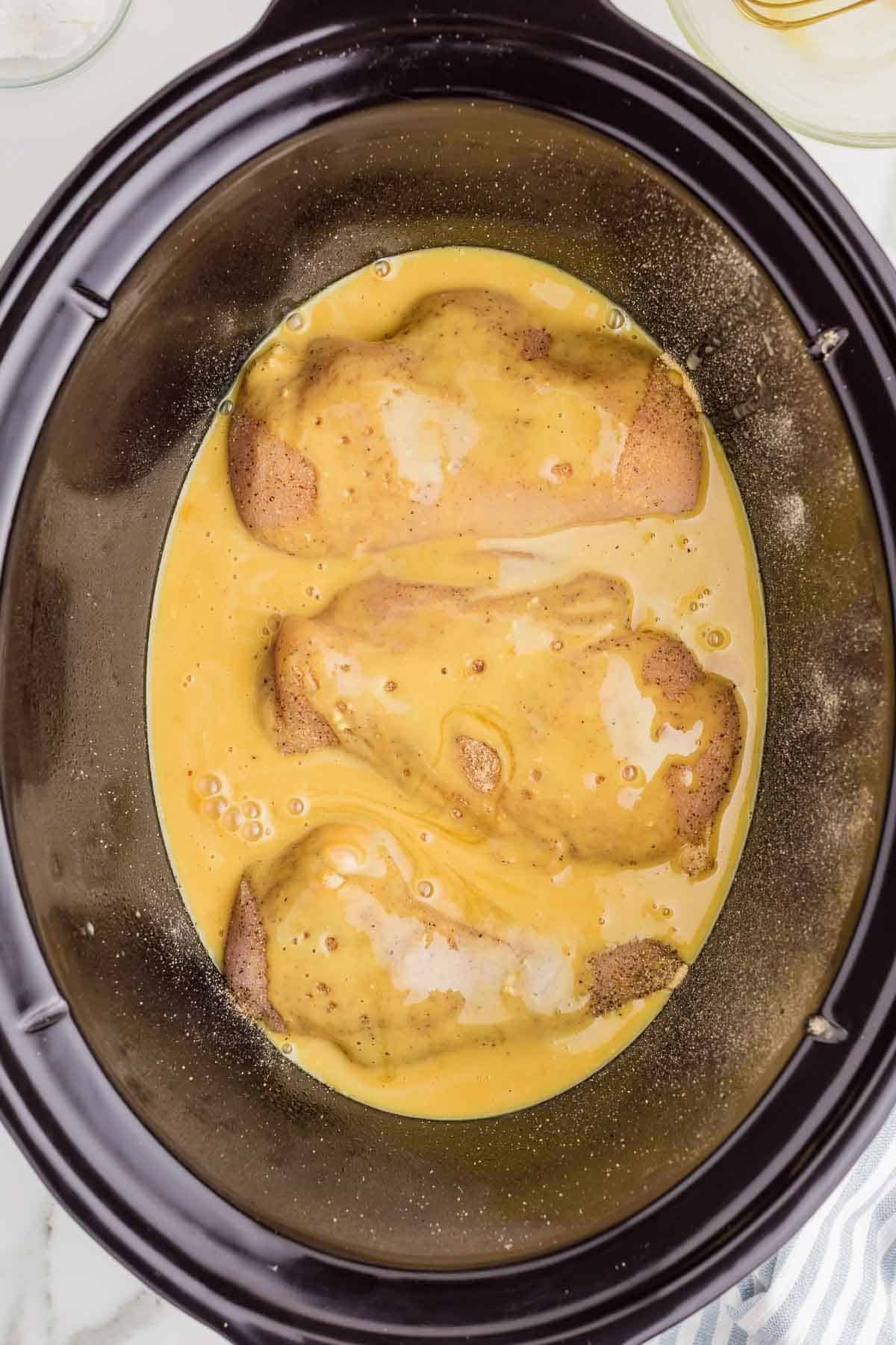 Seasoned chicken breasts in the slow cooker covered with a mixture of Dijon mustard. Honey. And chicken broth. The golden sauce surrounds each piece of chicken.