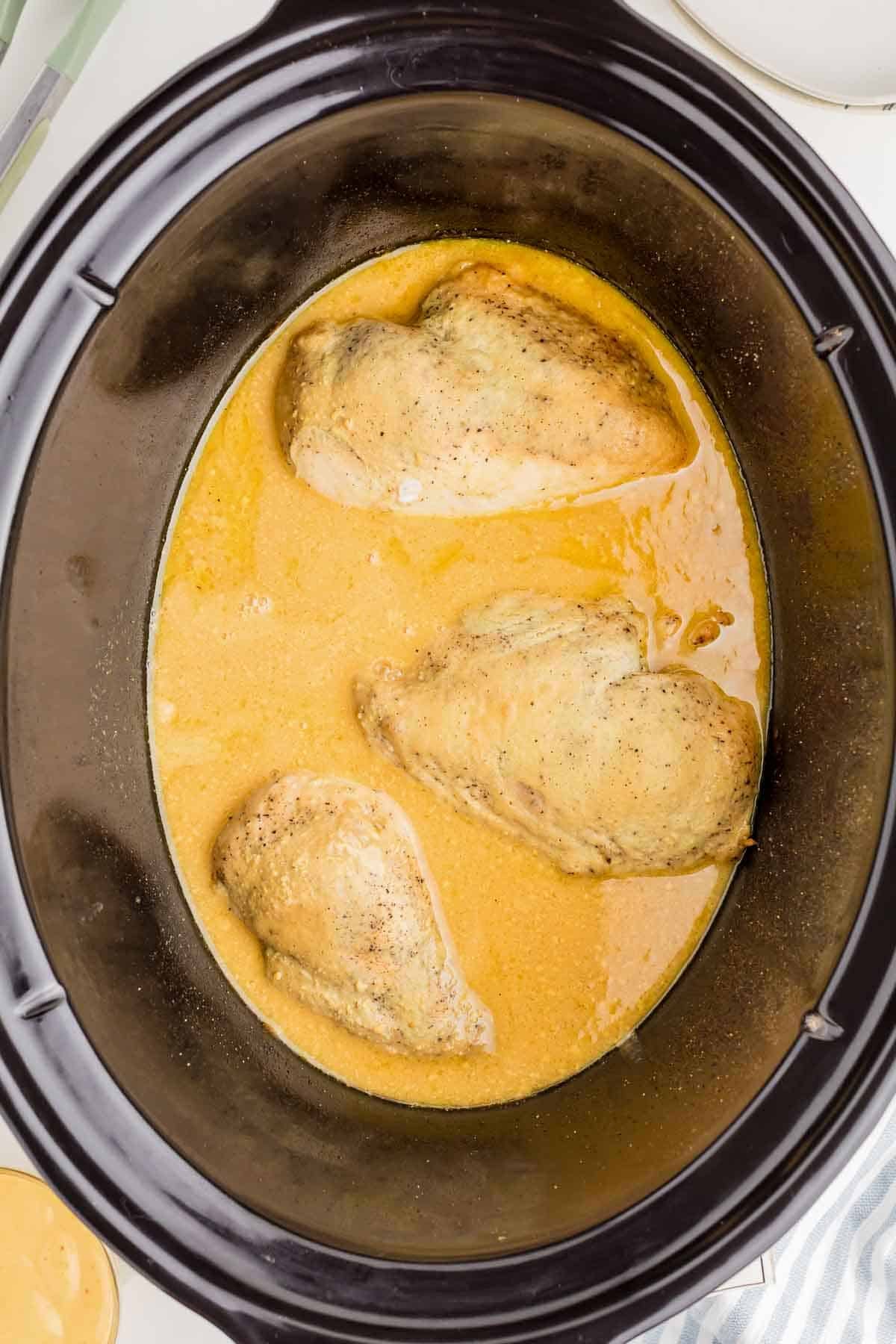 Cooked chicken breasts resting in honey mustard sauce inside the slow cooker. The chicken is ready to be removed and shredded.